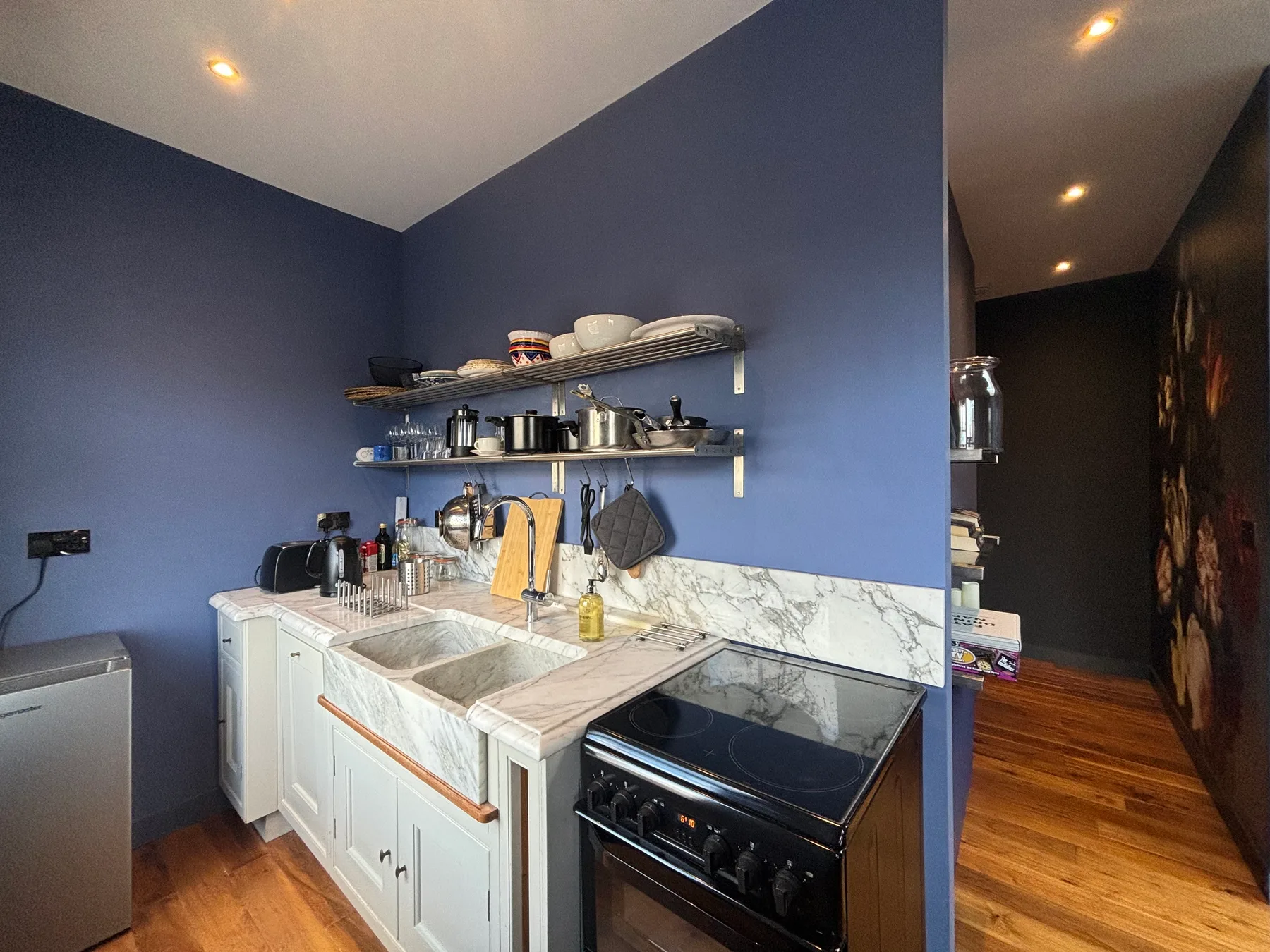 A compact kitchen with white cabinets, open shelves, and a dark stove.