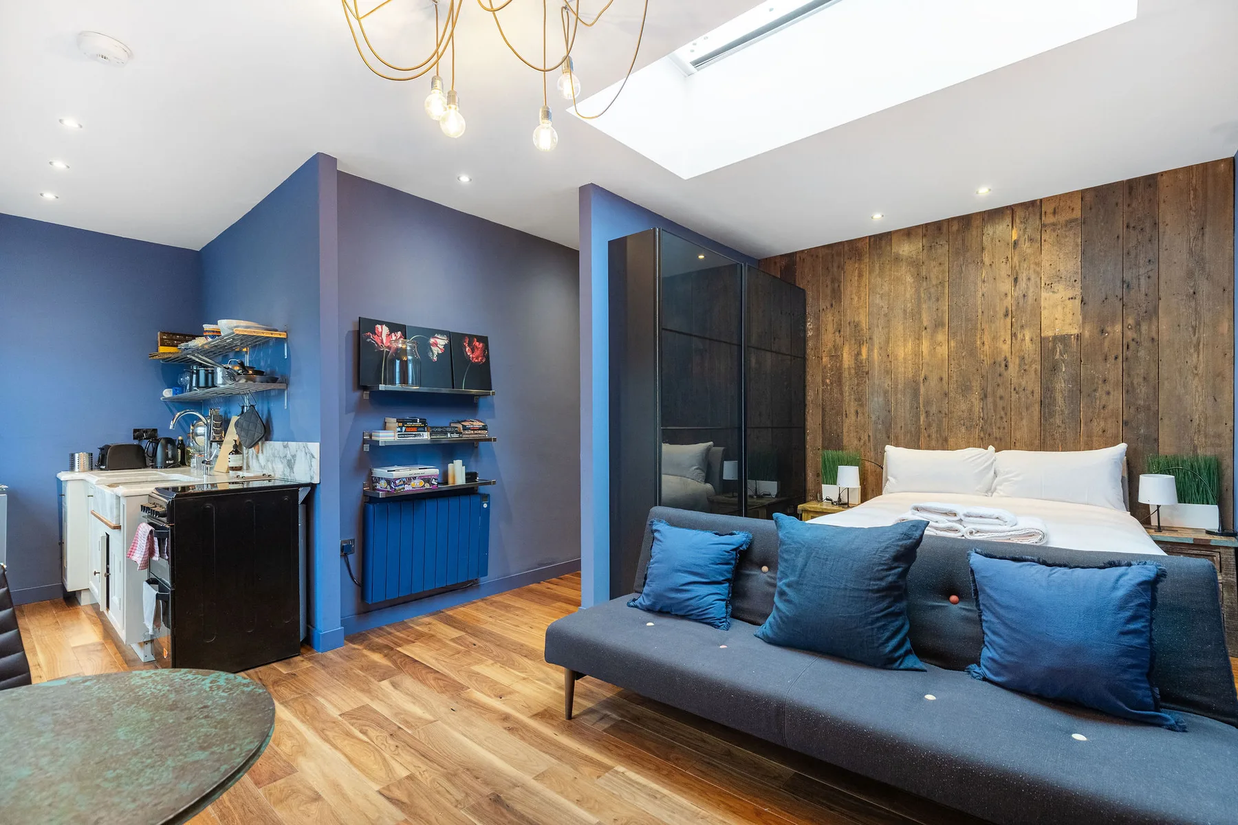 A bedroom with a bed, blue seating, and a kitchenette.
