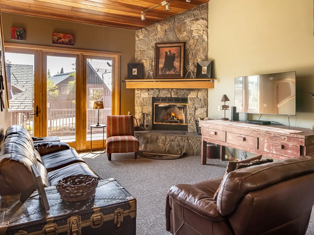 A living room with a stone fireplace, leather seating, and glass doors opening to a balcony.