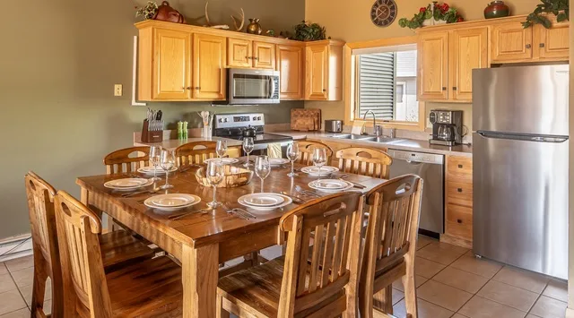 Una mesa de comedor de madera y sillas ocupan una cocina con gabinetes de madera y electrodomésticos.