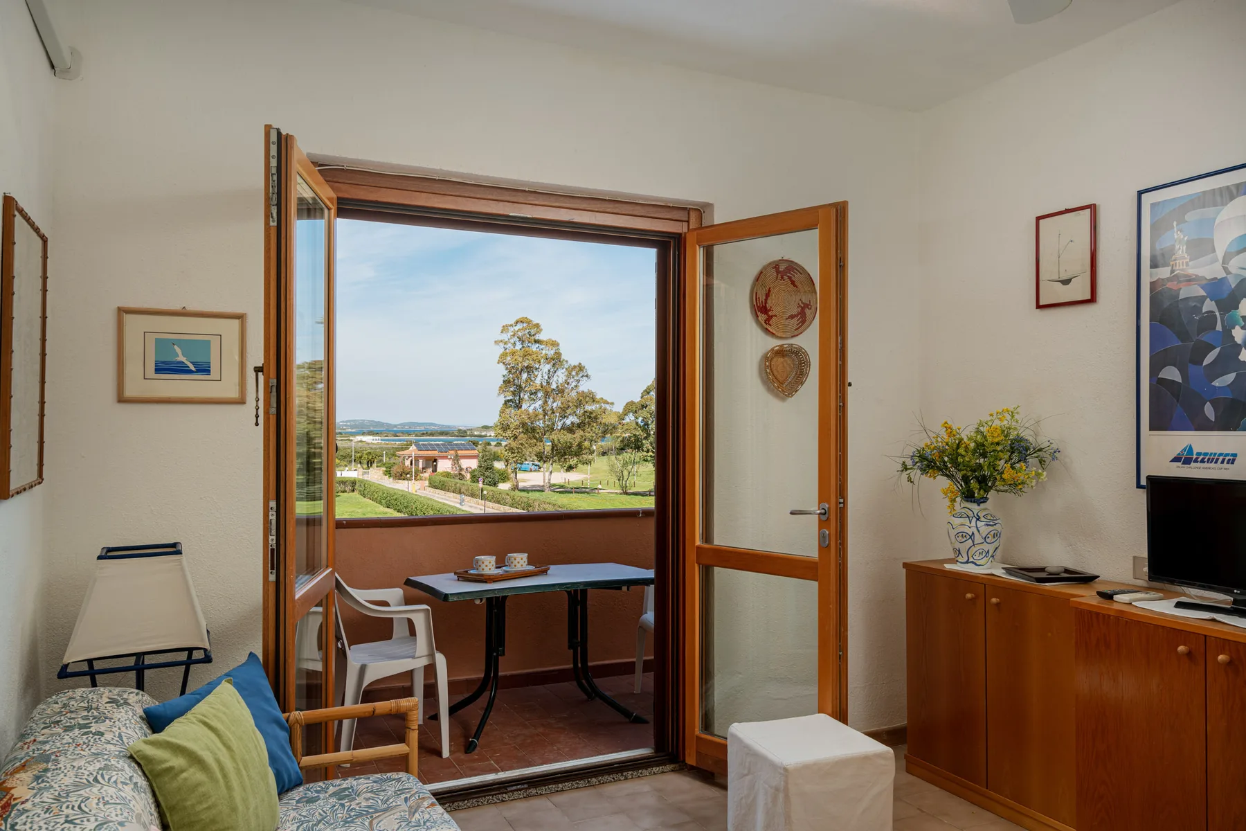 A bright living room opens through wooden doors to a balcony with a table and chairs.