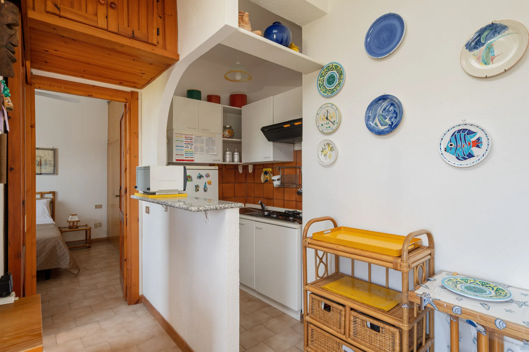 A compact kitchen with a white counter and colorful plates displayed on the wall.