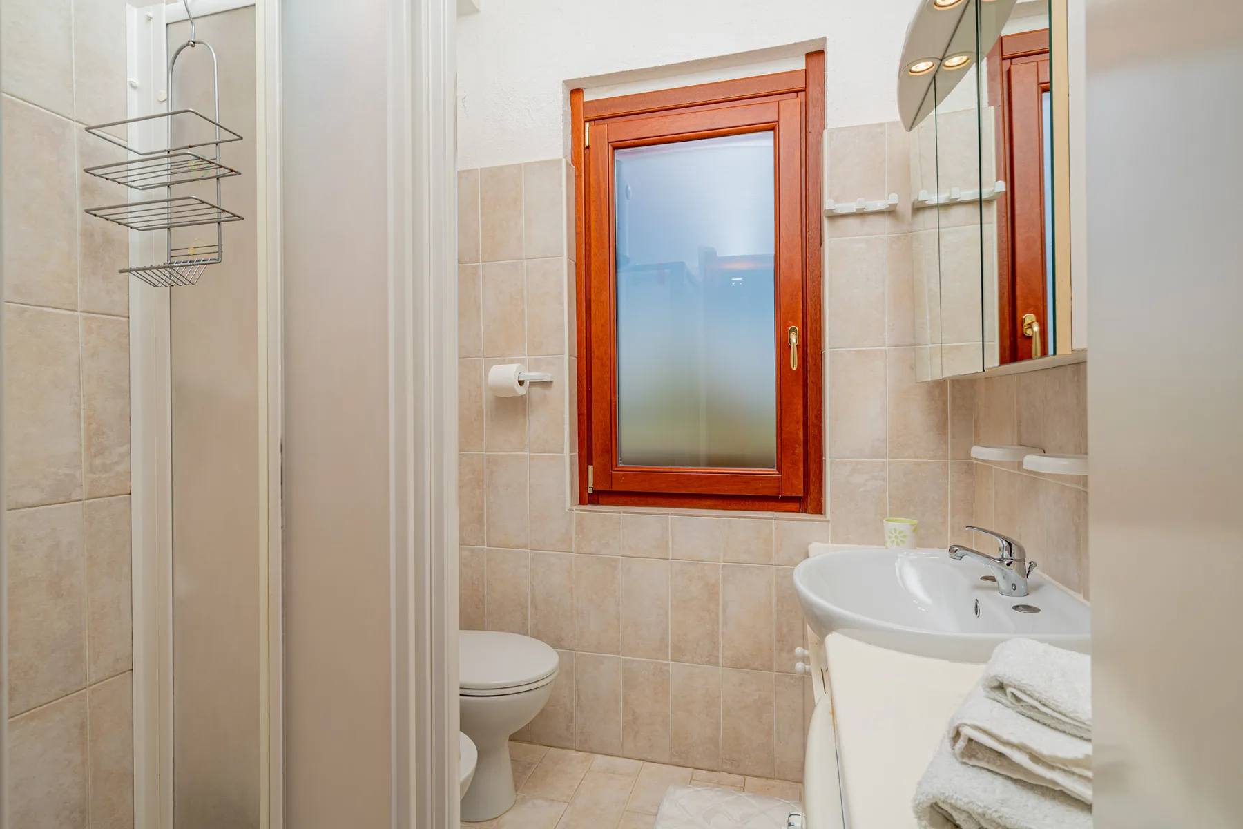 A tiled bathroom with a shower, toilet, and sink beneath a window.