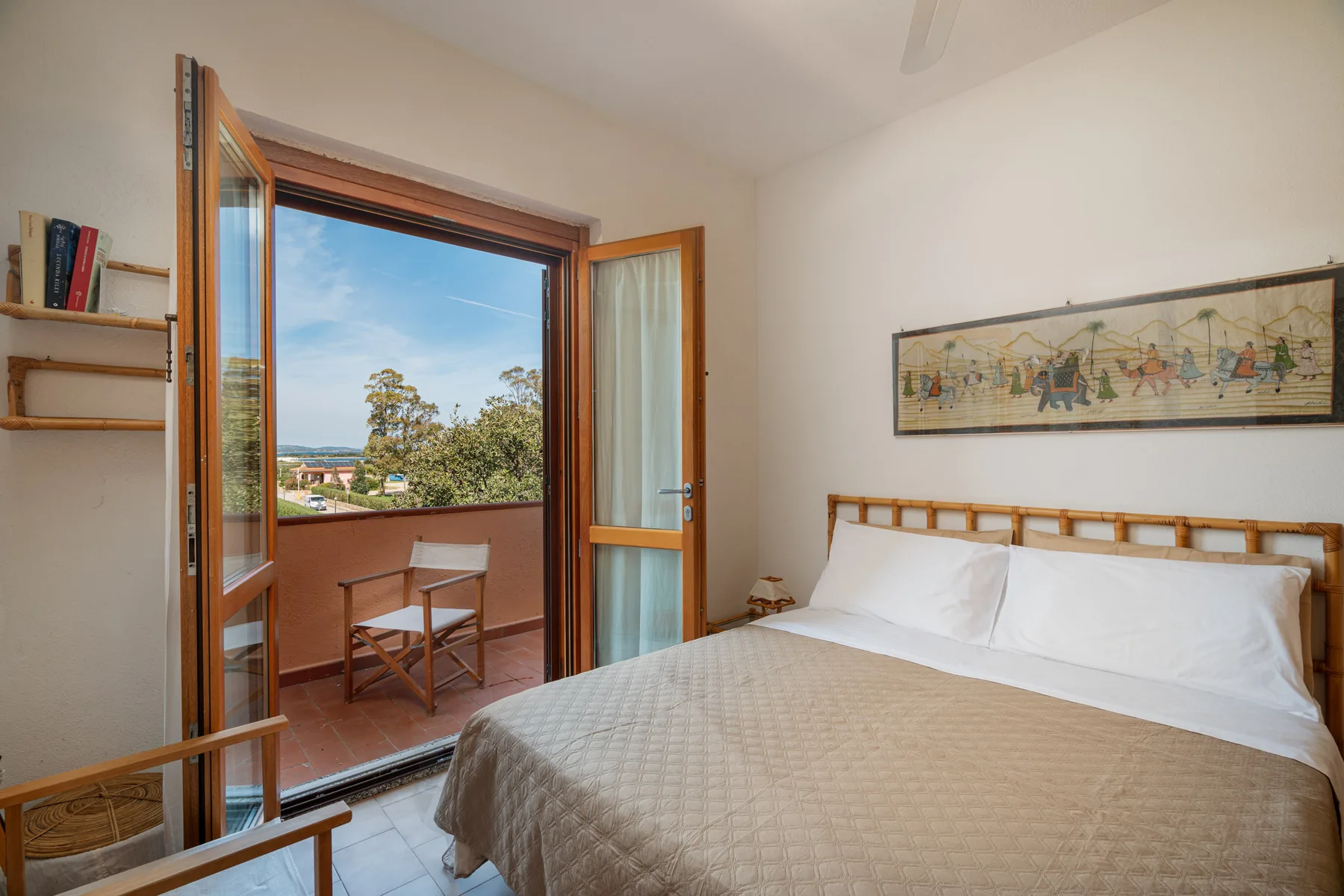 A bedroom with a bed beside open glass doors leading to a balcony.