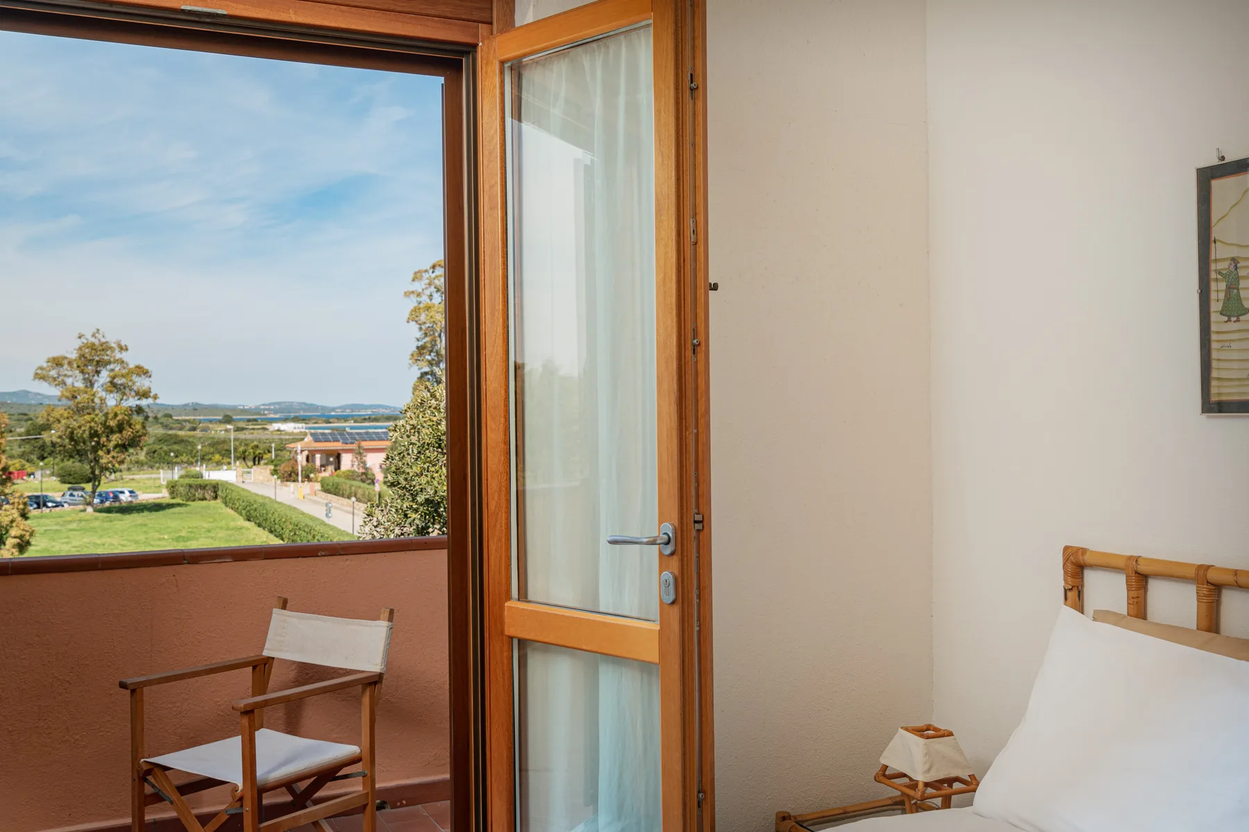 A bedroom opens onto a balcony with a view of trees and distant buildings.