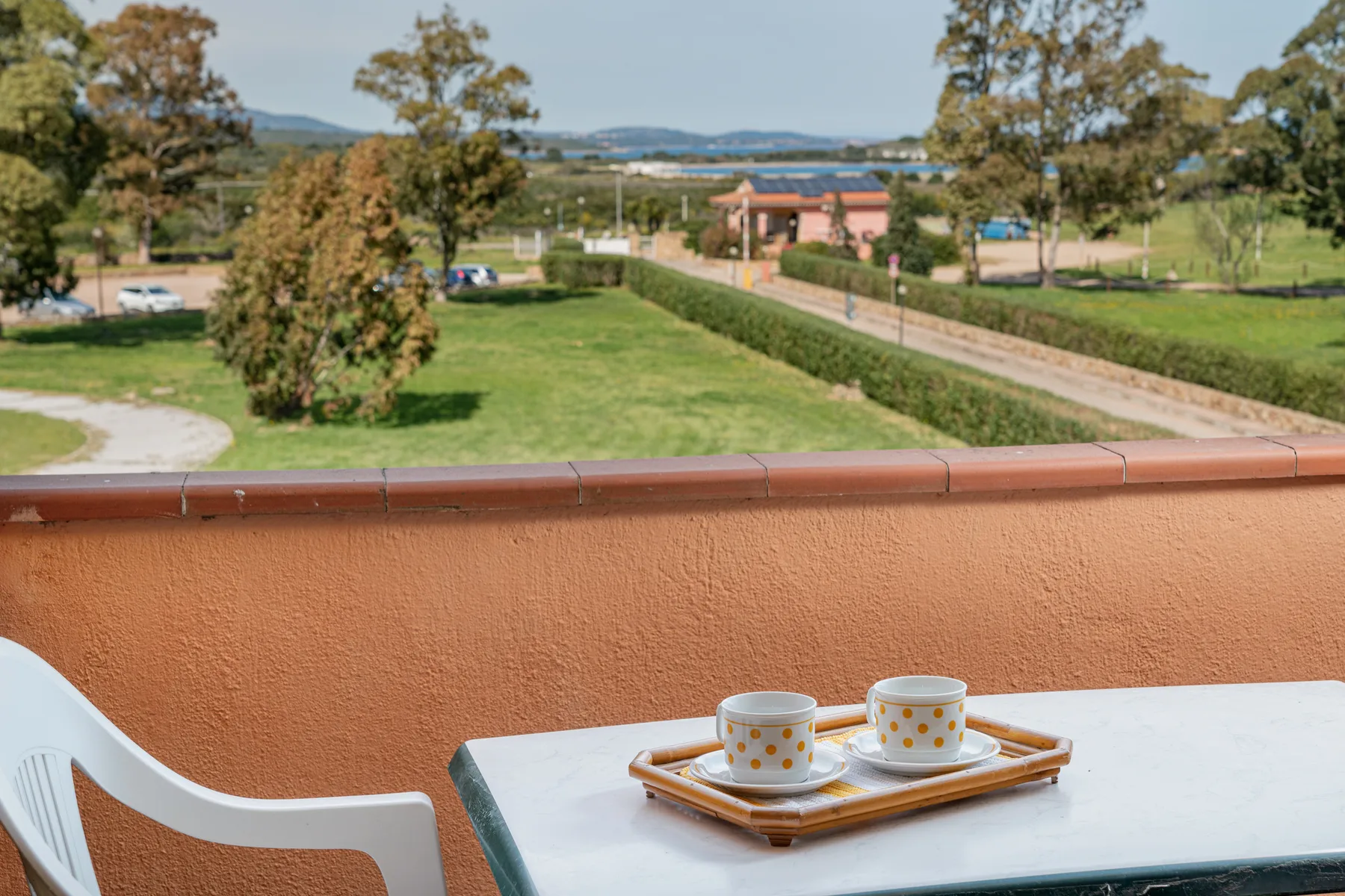 A patio table with cups overlooks a grassy landscape and a road.