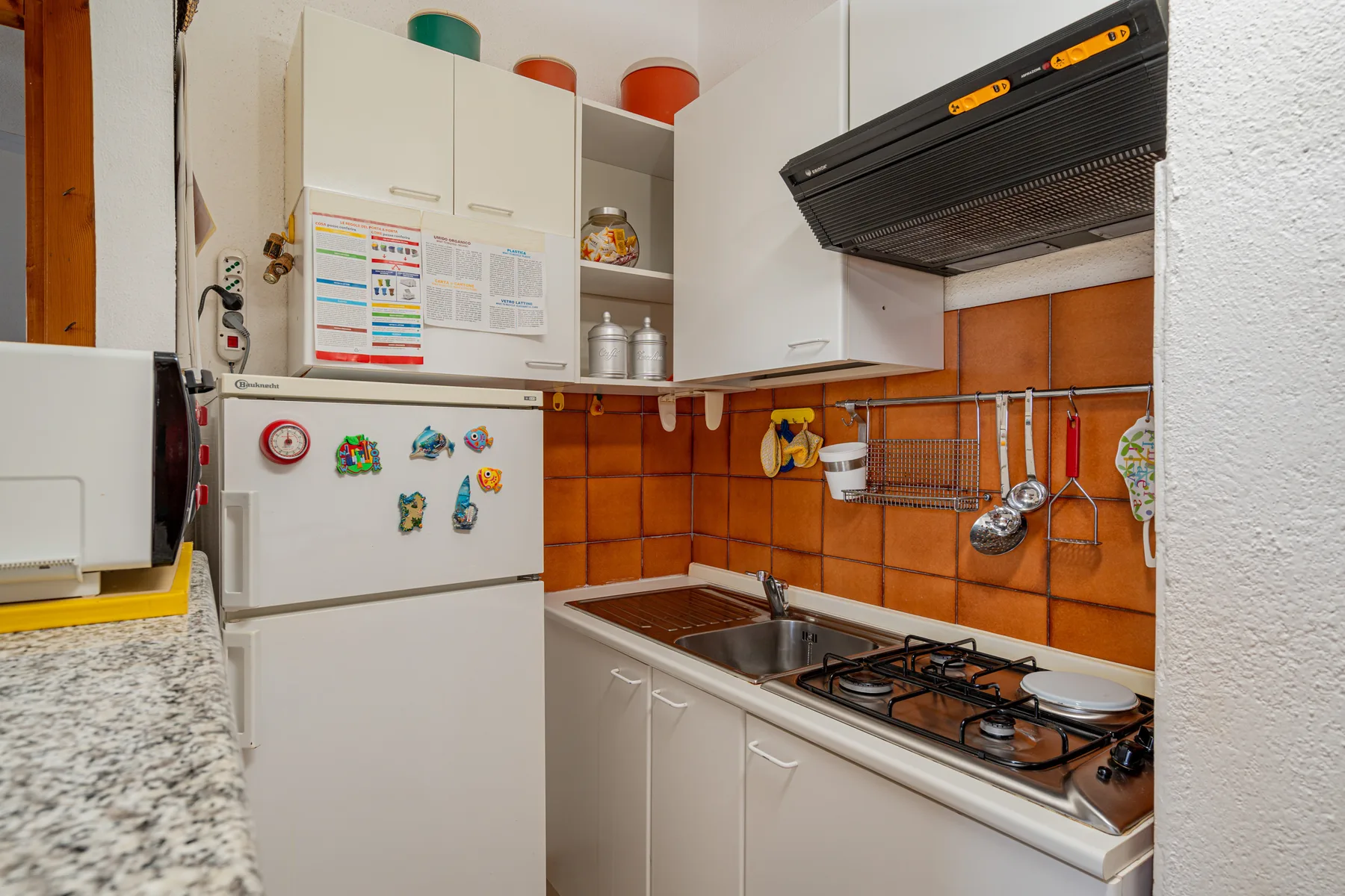 A compact kitchen with white cabinets, a refrigerator, and a gas cooktop.
