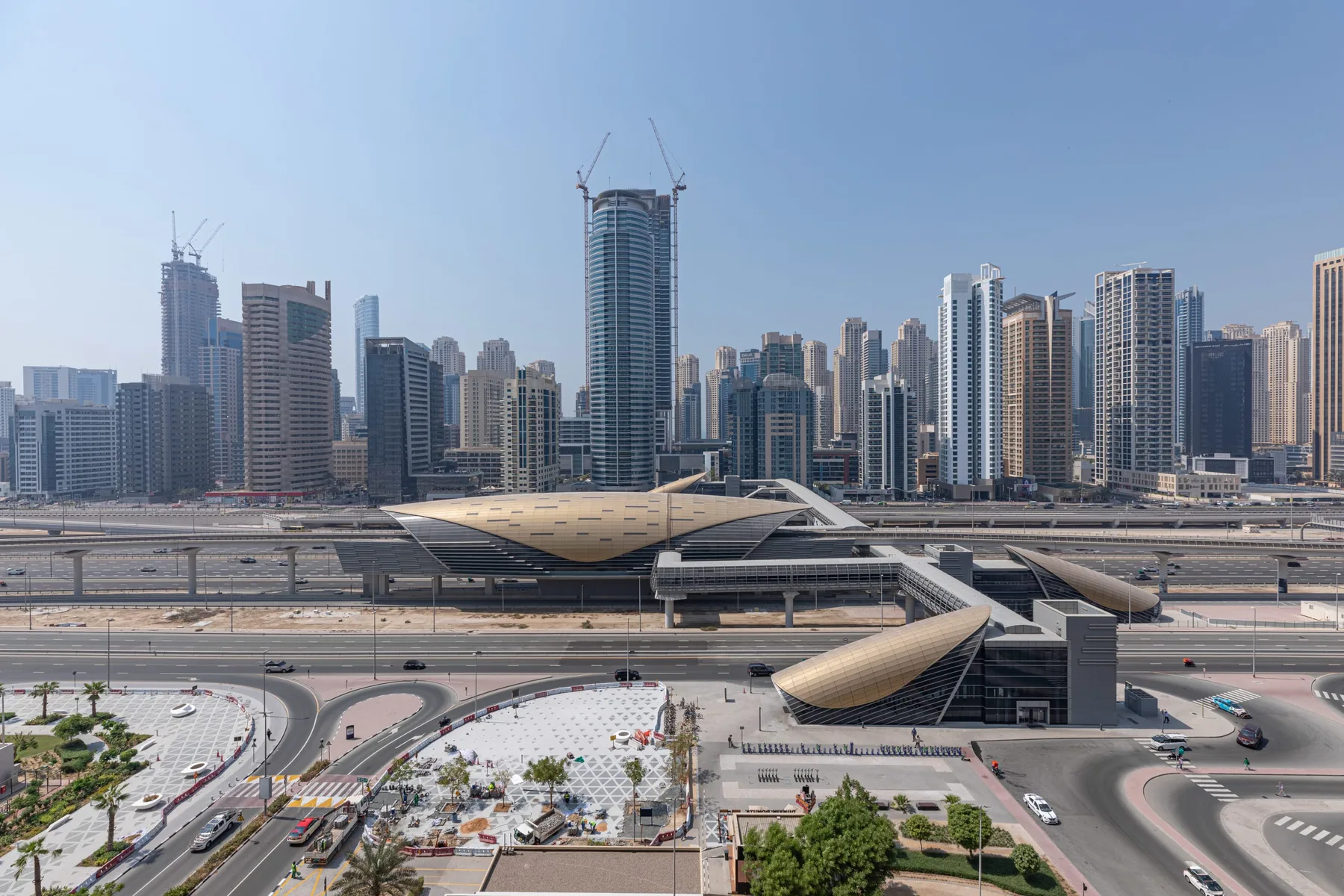 Una estación de transporte moderna y las calles circundantes se encuentran frente a un denso horizonte urbano.