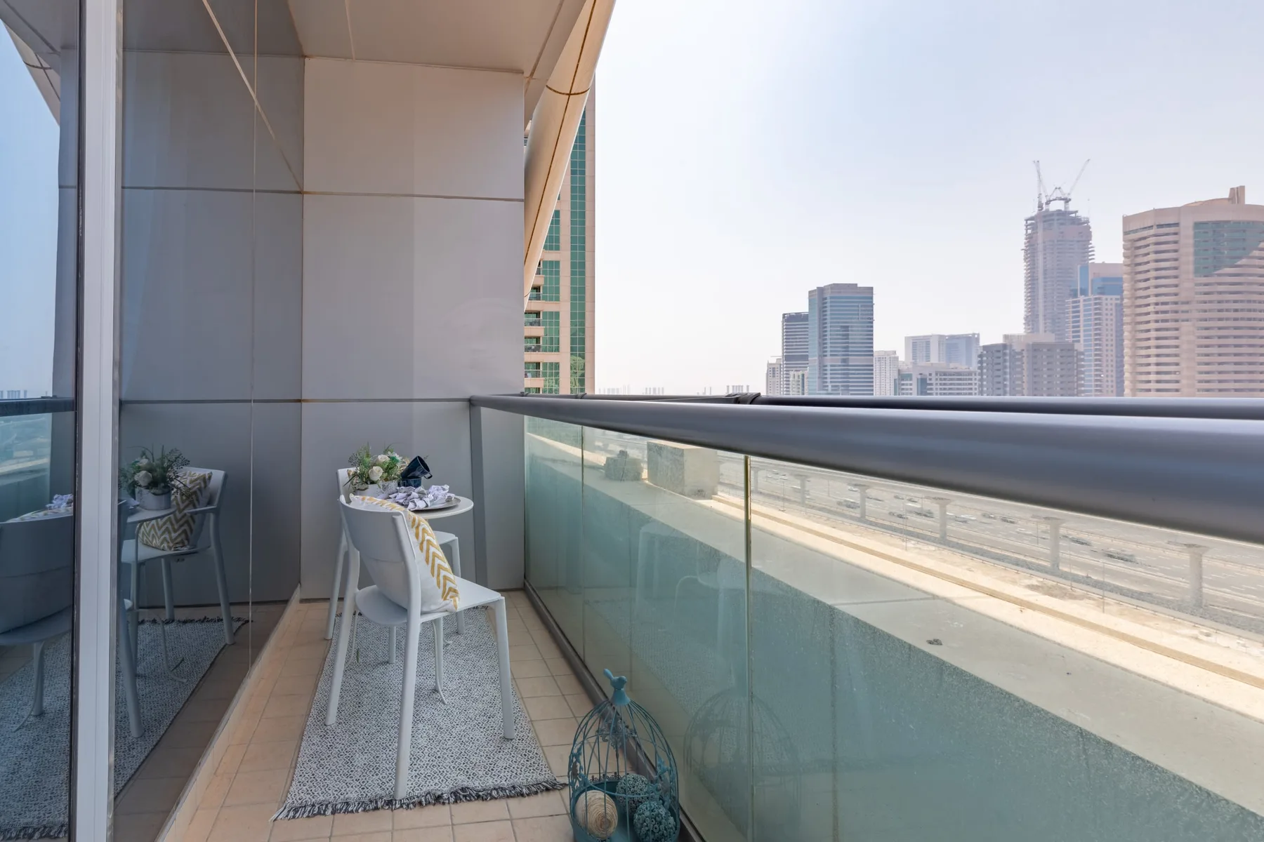 Un balcón con una mesa pequeña y sillas da a un horizonte urbano.