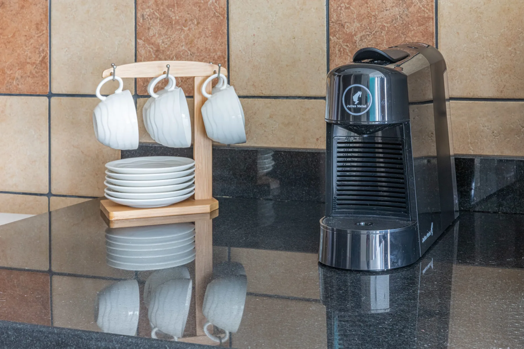 Una estación de café con una cafetera de cápsulas, tazas colgadas y platos apilados.