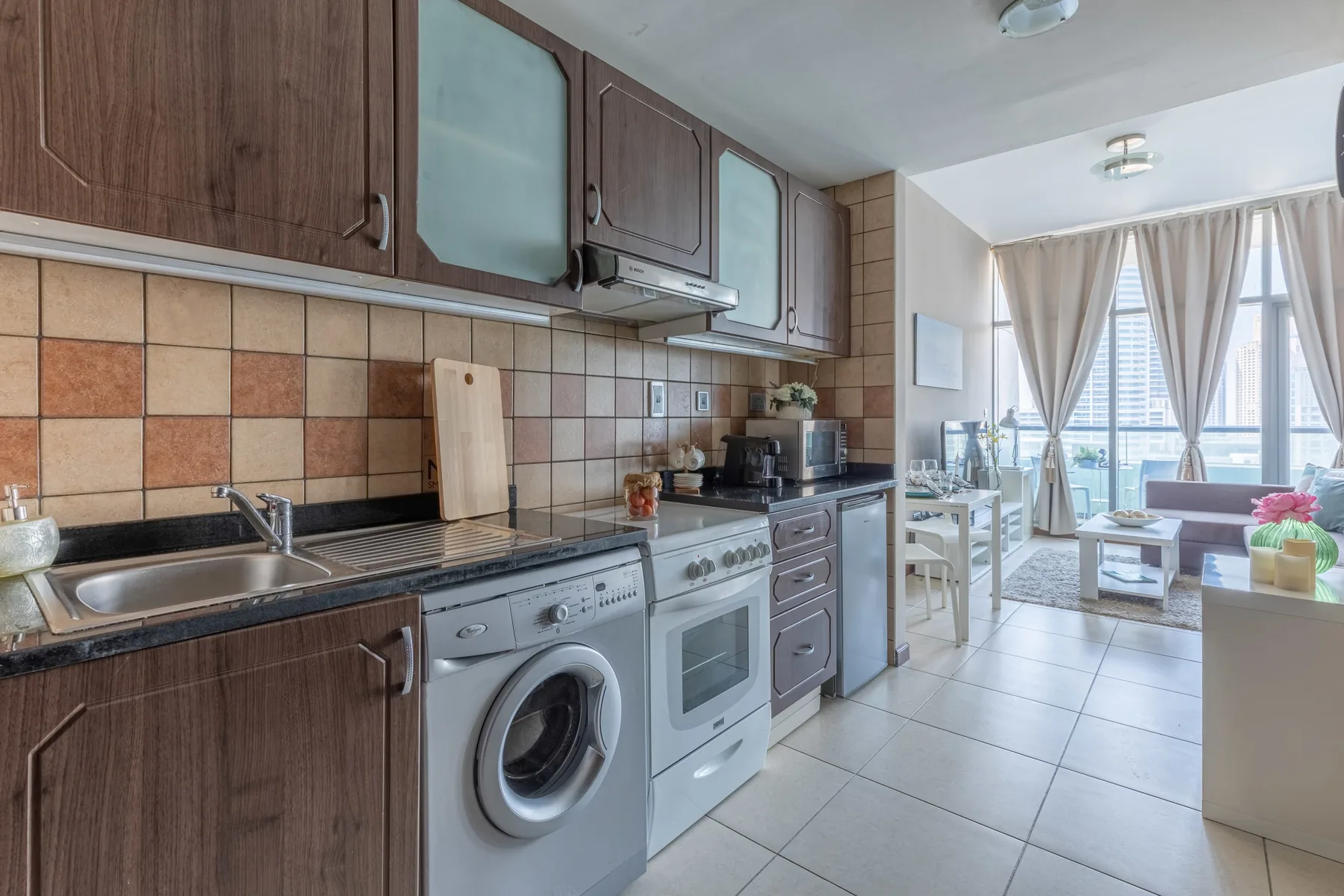 Una cocina con gabinetes de madera y lavadora se abre a un comedor luminoso.