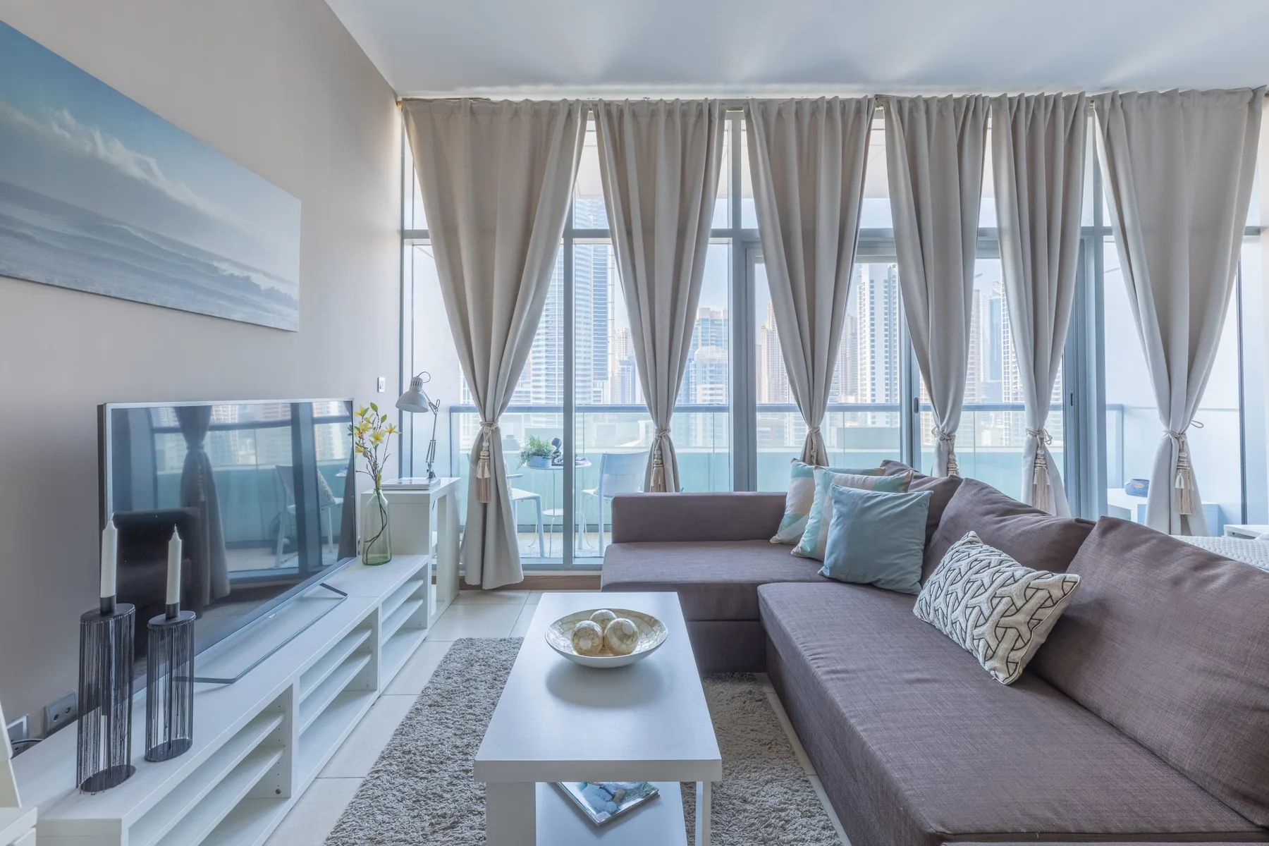 Sala de estar con sofá seccional, mesa de centro y grandes ventanas con cortinas.