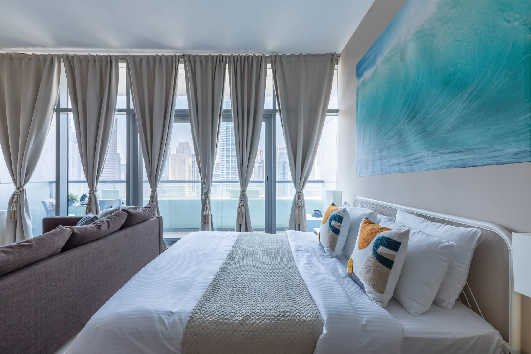 Un dormitorio con una cama grande, cortinas grises y una pintura colorida en la pared.
