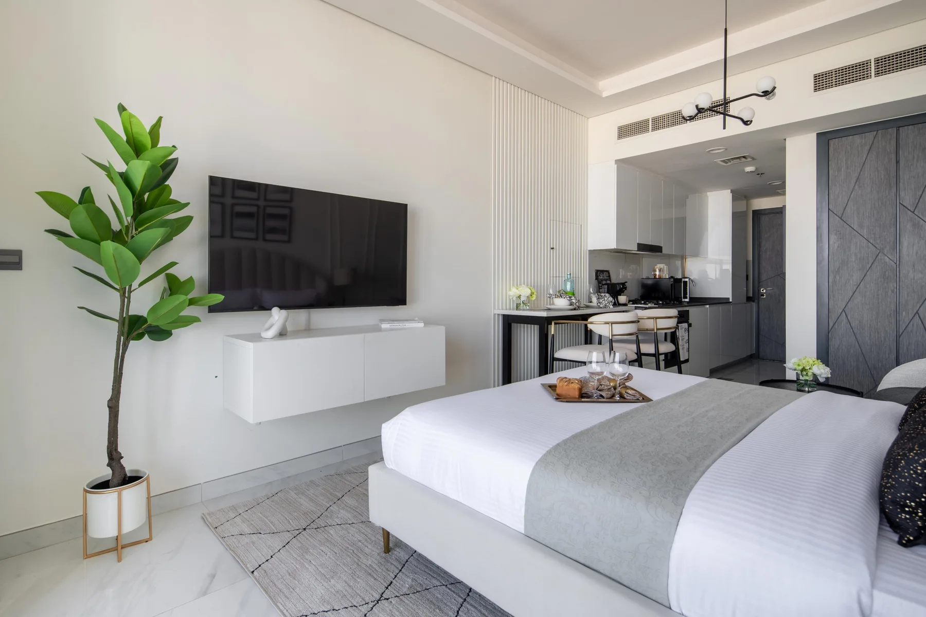 Un dormitorio luminoso con una cama bien tendida y una pequeña zona de cocina.
