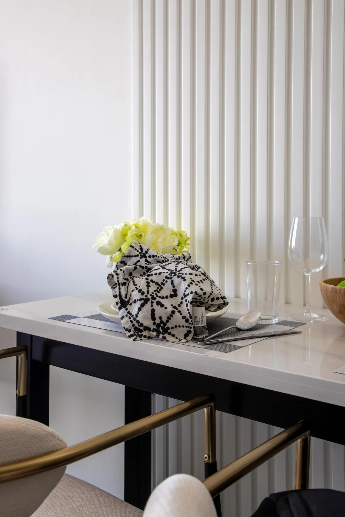 A bright dining table holds a vase of flowers and clear glassware.