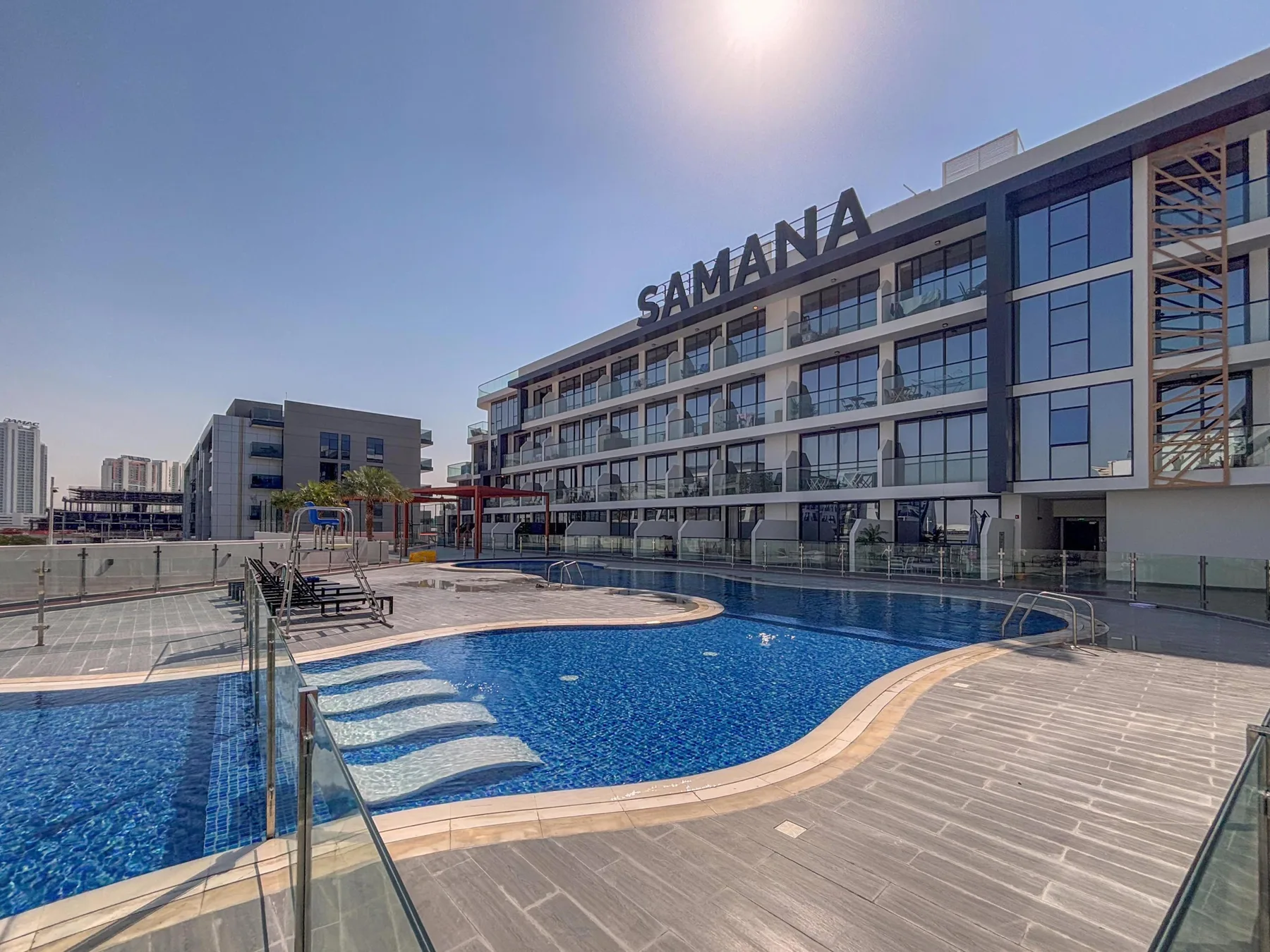 Una piscina y una terraza embaldosada están frente a un edificio moderno de varios pisos.
