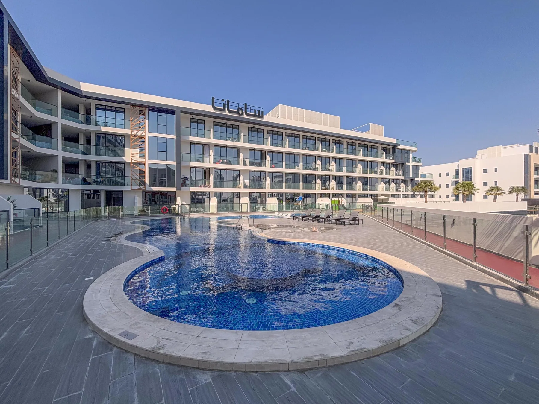 Un edificio hotelero da a una piscina azul y una terraza pavimentada.