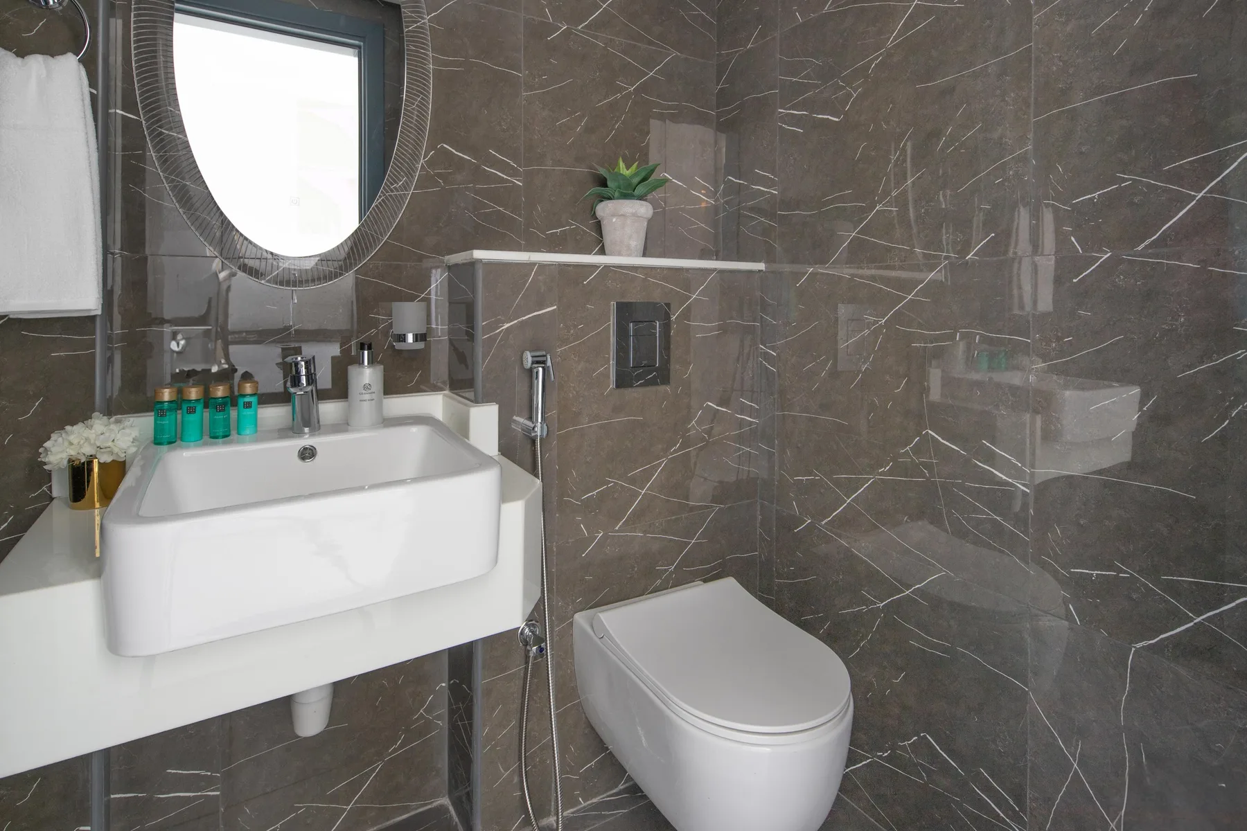 Baño con paredes de azulejos, lavabo, inodoro y mampara de ducha de vidrio.