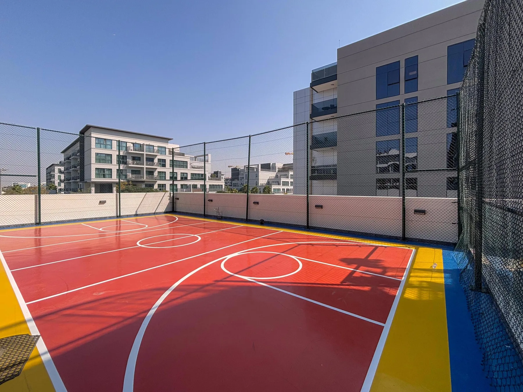 Una cancha deportiva al aire libre con superficie roja y líneas blancas.
