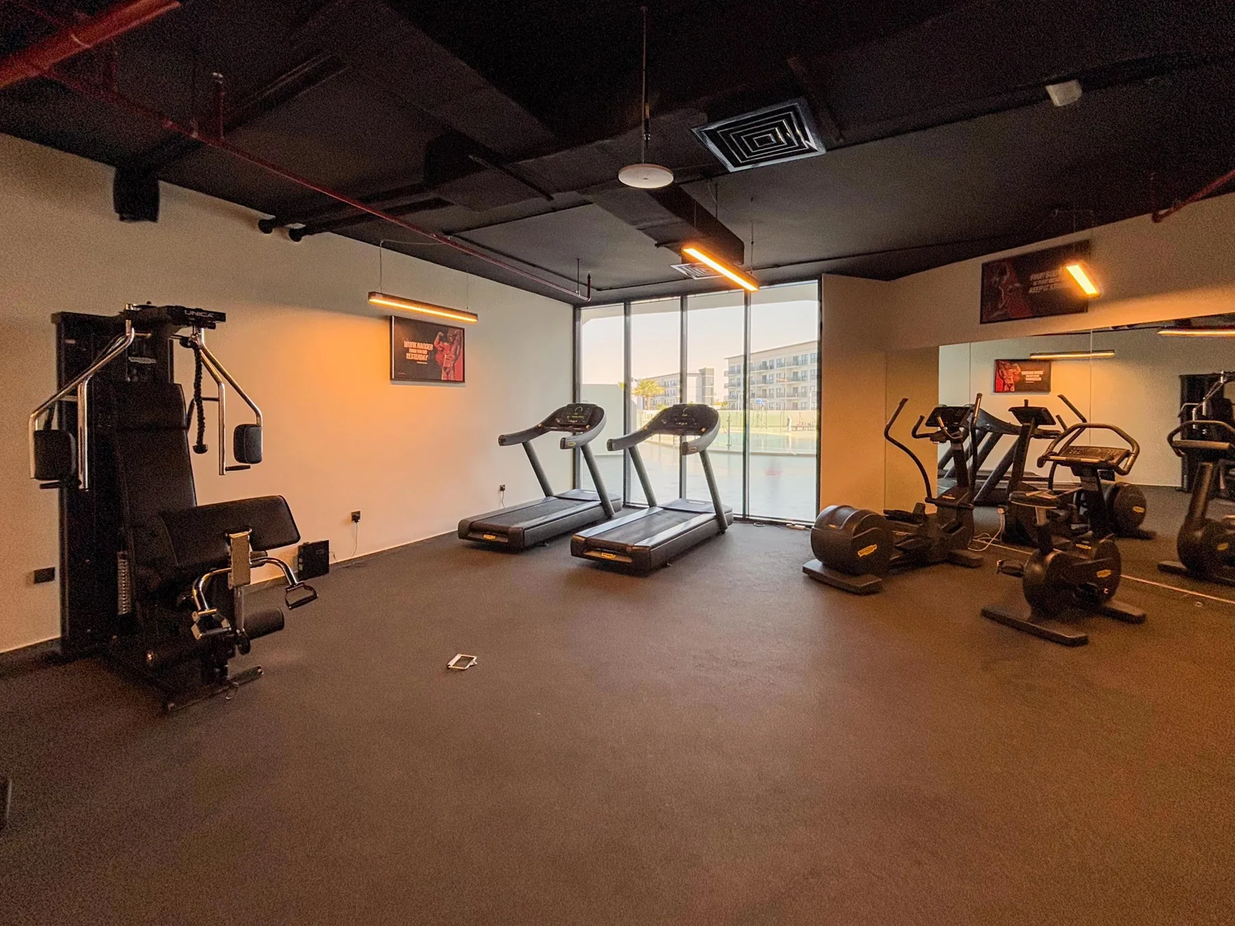 Un gimnasio con cintas de correr y máquinas de entrenamiento junto a grandes ventanales.