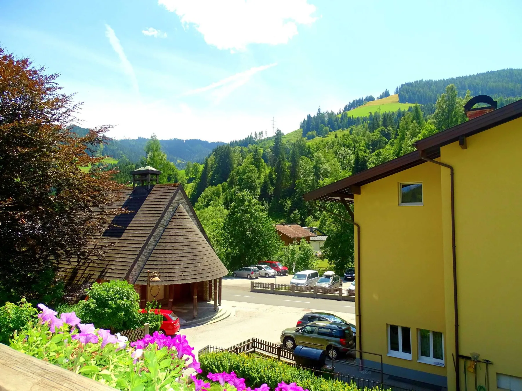 A mountain resort scene with a yellow building, parked cars, and wooded hills.