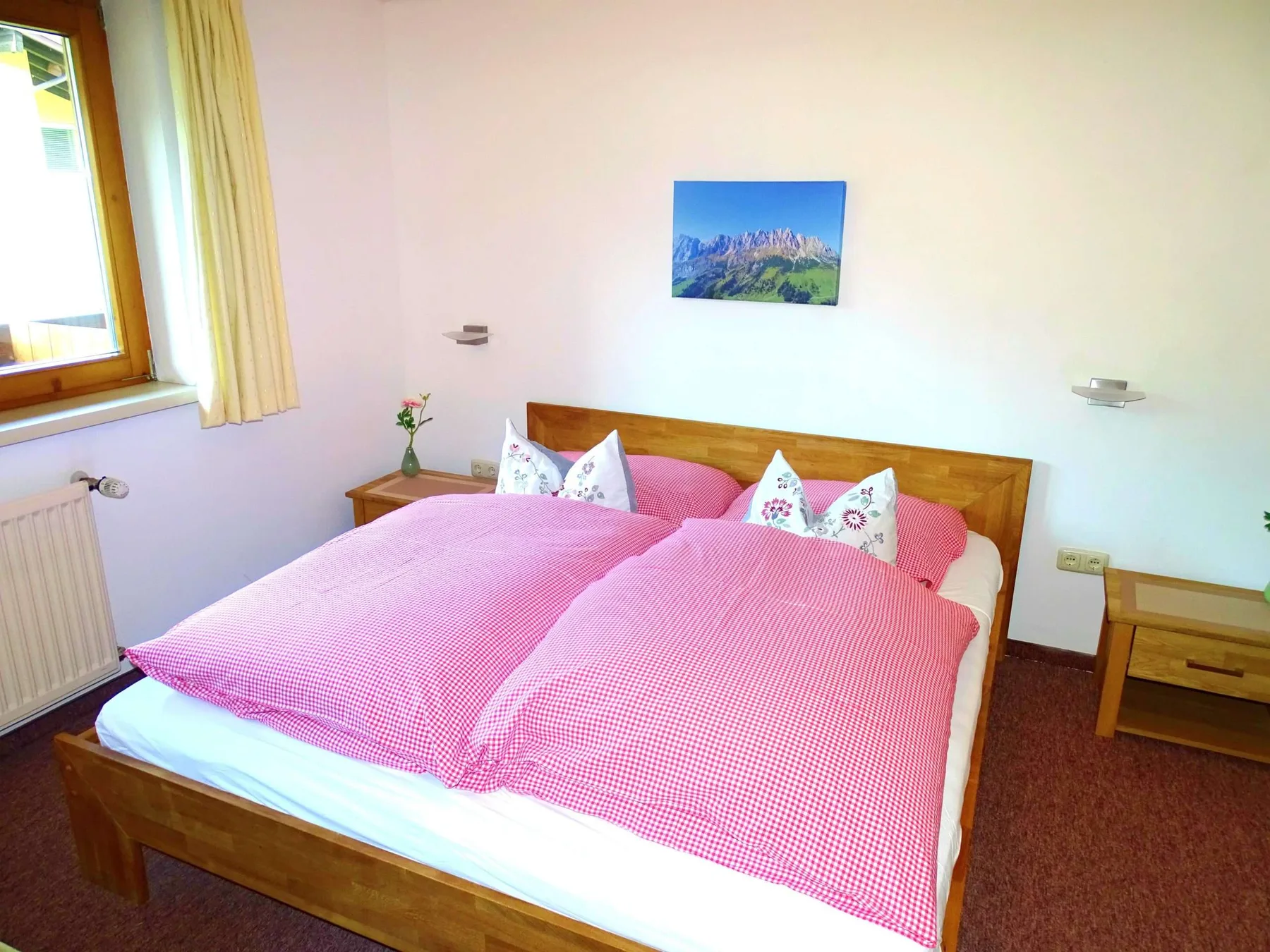 A bedroom with a wooden bed dressed in pink bedding and pillows.