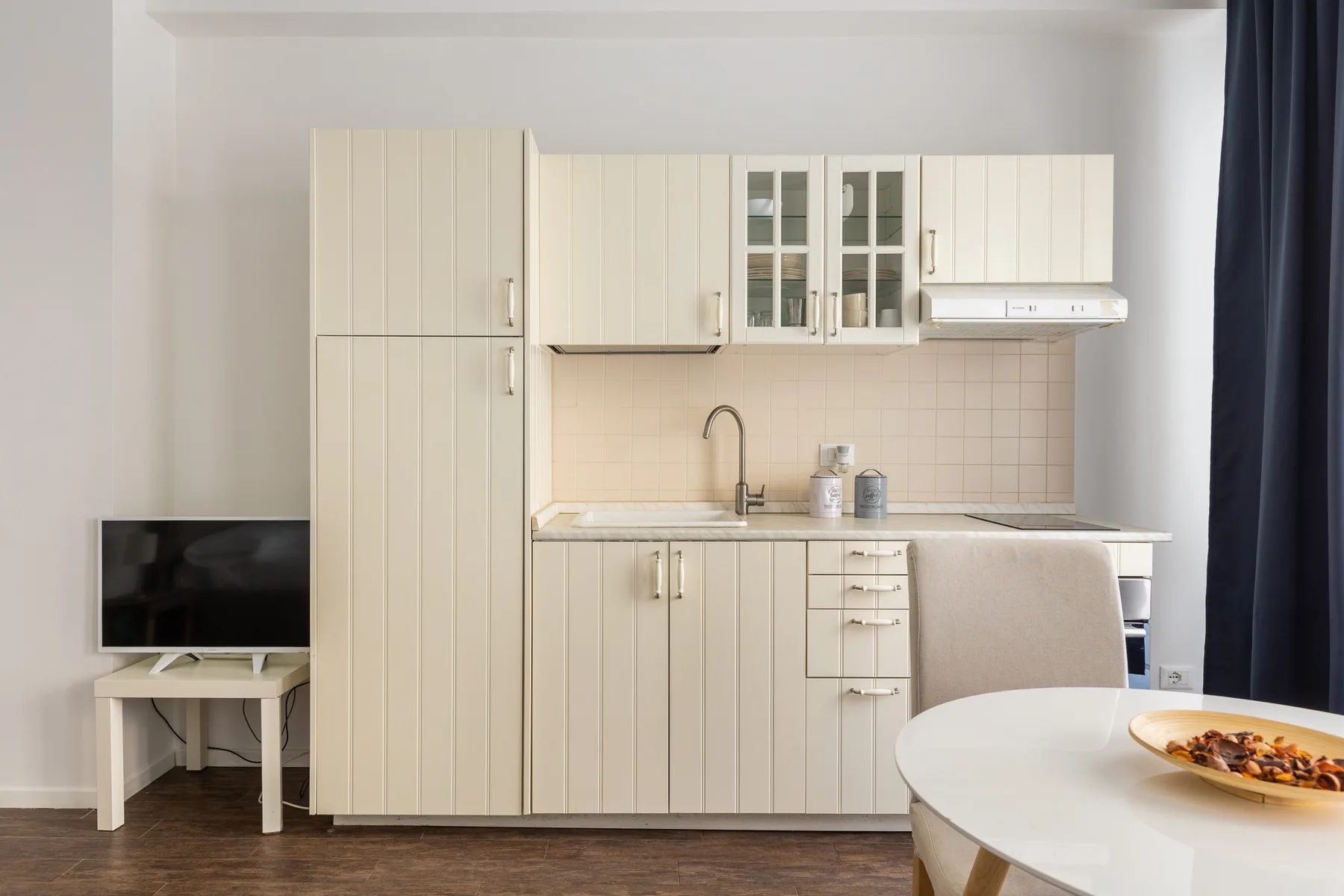 A compact kitchen with pale cabinets, a sink, and a dining table.