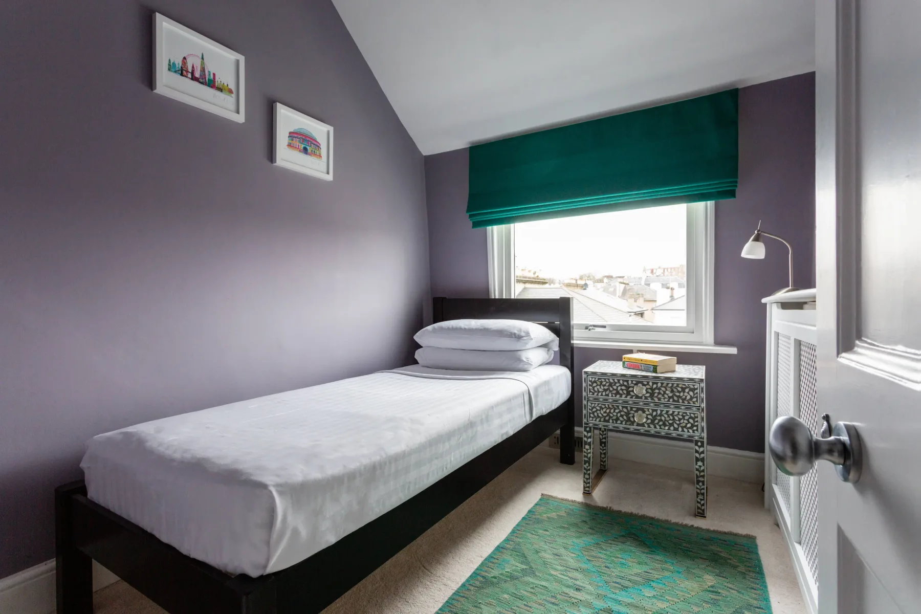 A bedroom with a single bed, a window, and a small table.