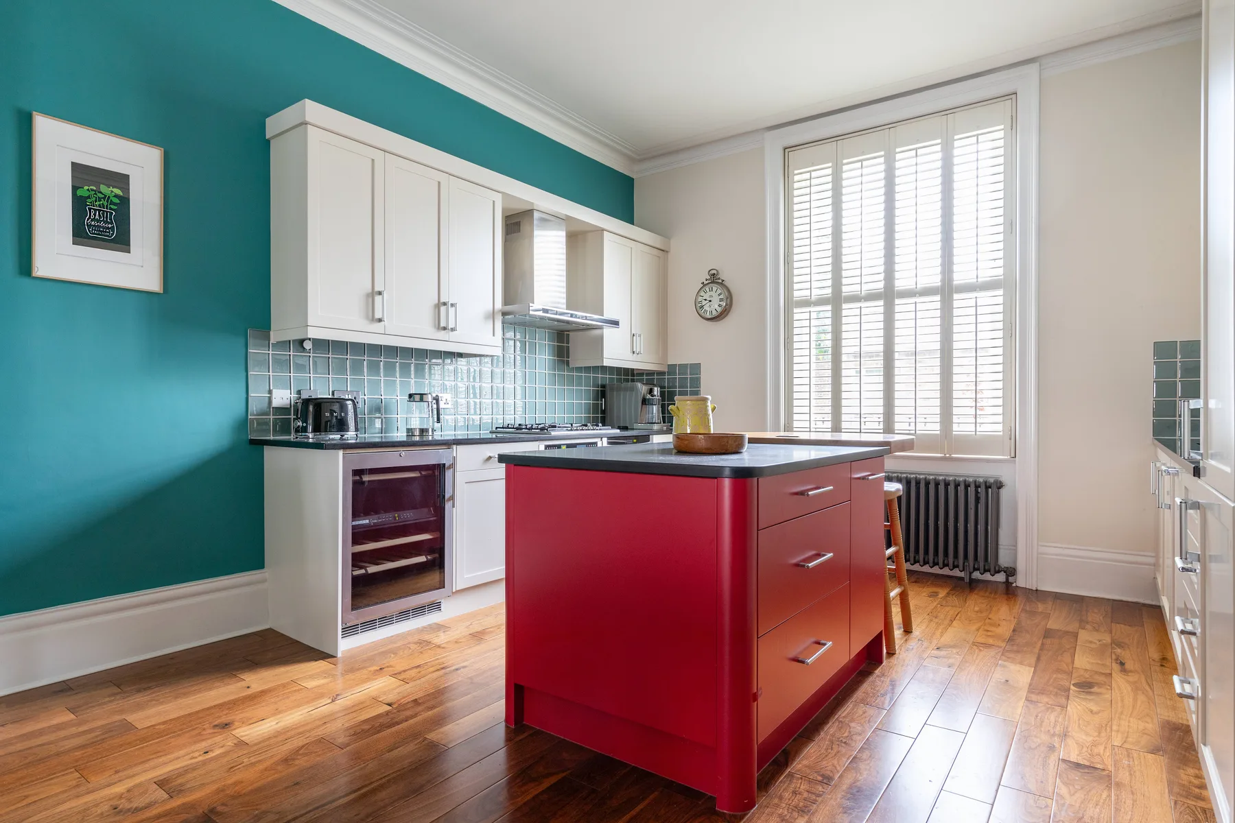 A bright kitchen with white cabinets, a red island, and large windows.