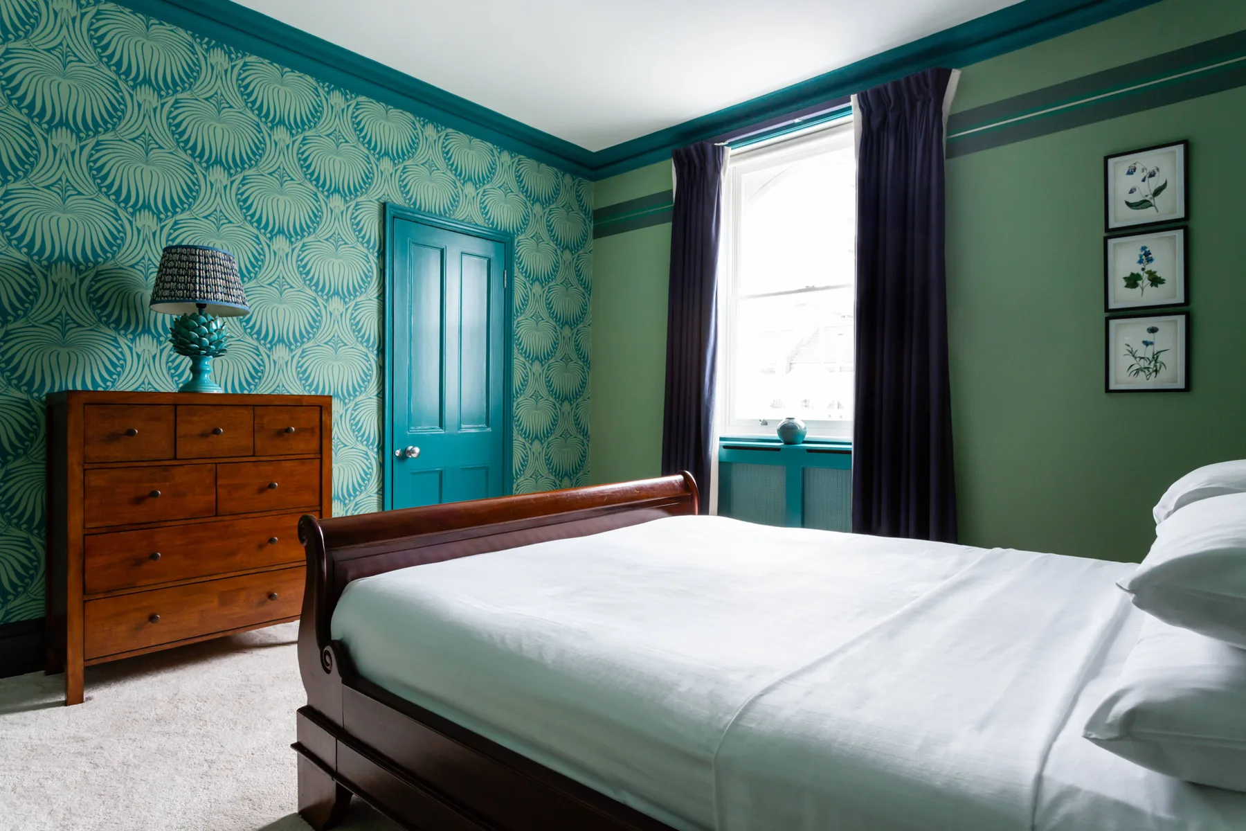 A bedroom with a wooden bed, patterned wallpaper, and a bright window.