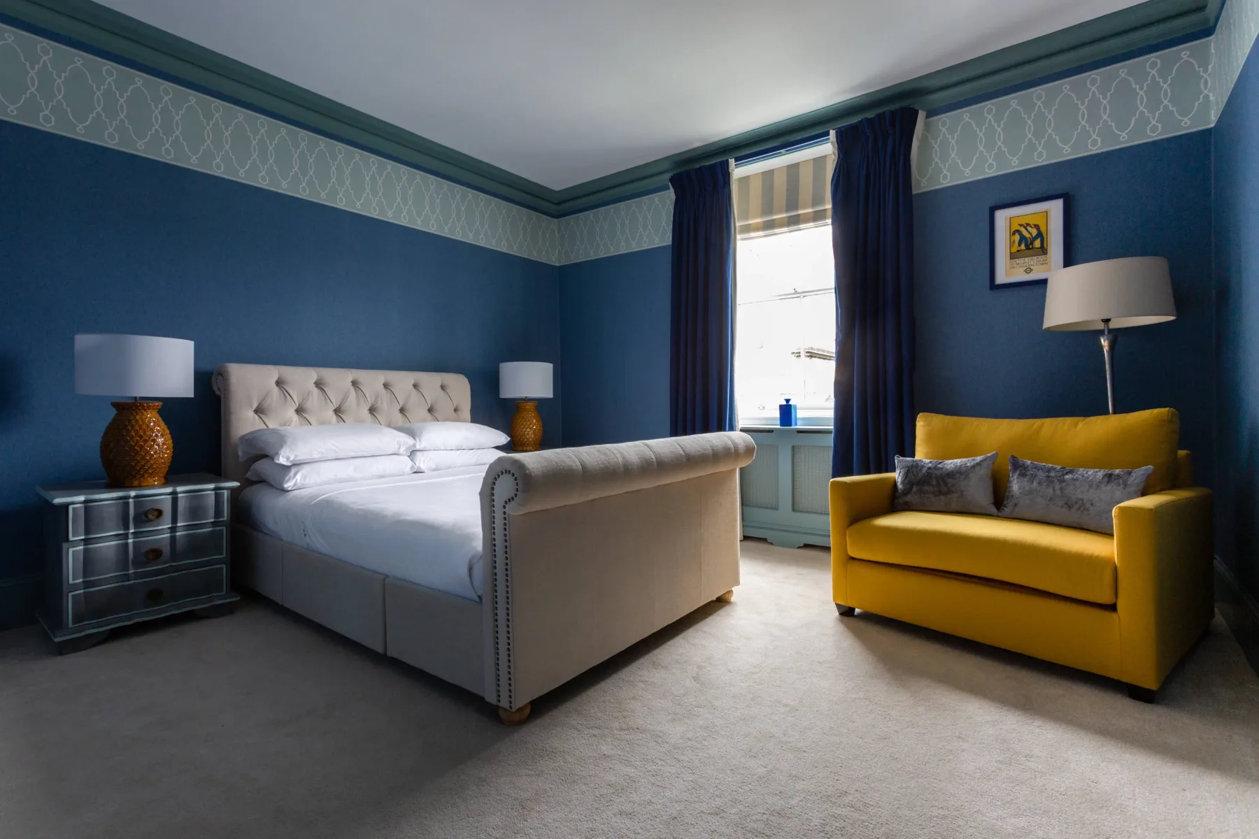A bedroom with a bed and a yellow sofa beside the window.