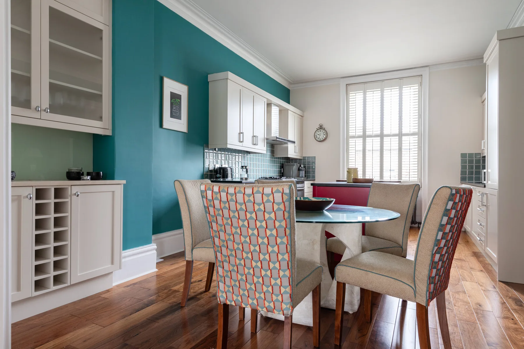 A dining area with a table and chairs beside a teal kitchen wall.