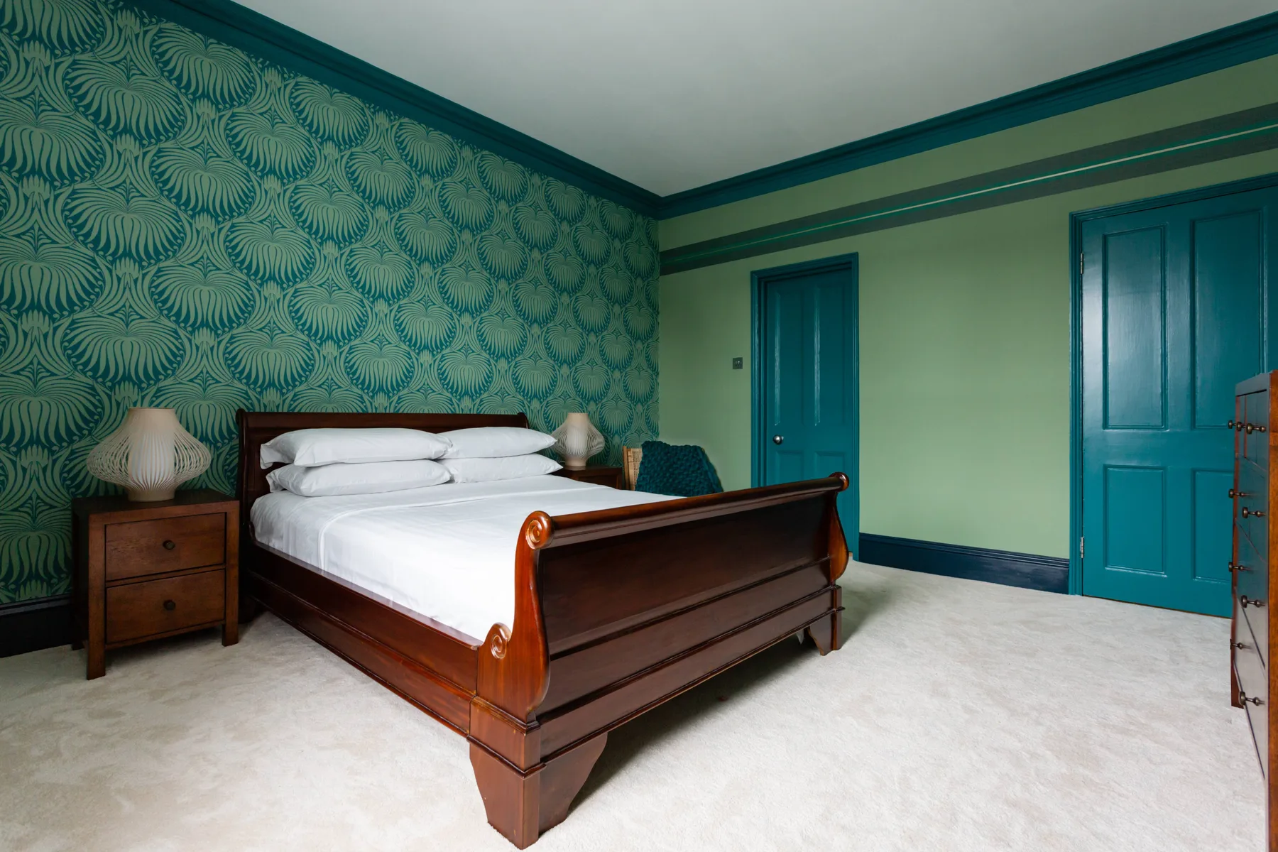 A bedroom with a wooden bed, patterned wallpaper, and teal doors.