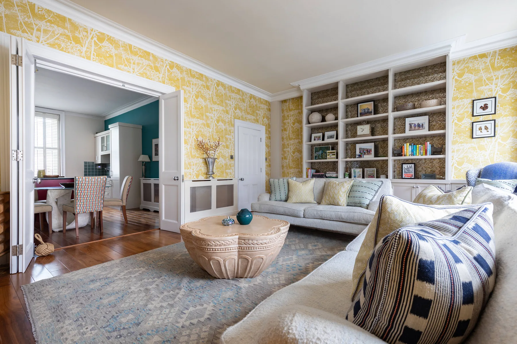 A living room with a sectional seating area, patterned wallpaper, and built-in shelves.