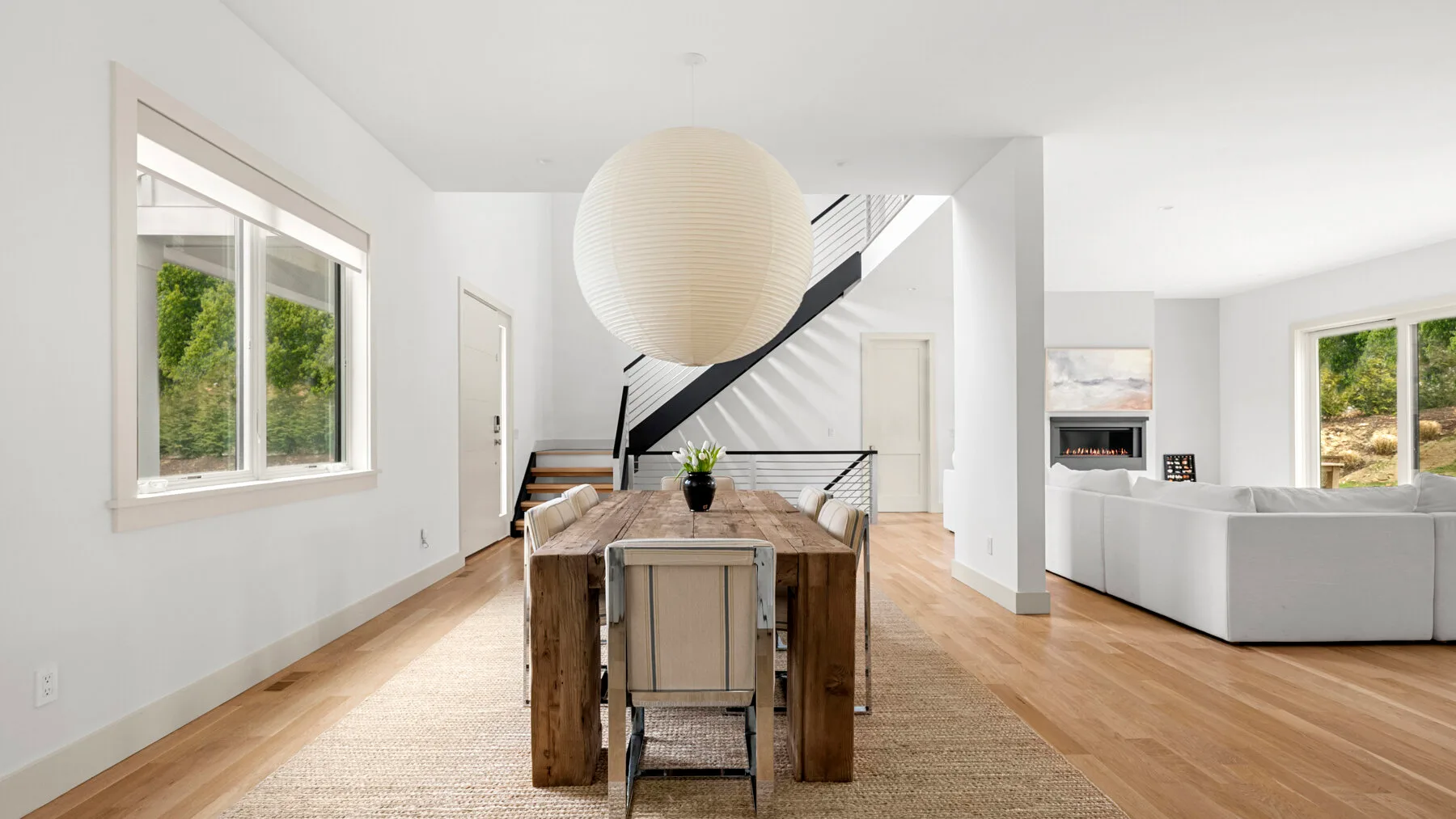 Un comedor y sala de estar luminosos y diáfanos, con una mesa de madera y grandes ventanas.