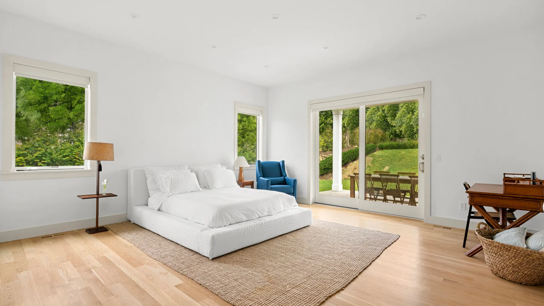 Un dormitorio luminoso con una cama blanca y ventanas con vistas a la vegetación.