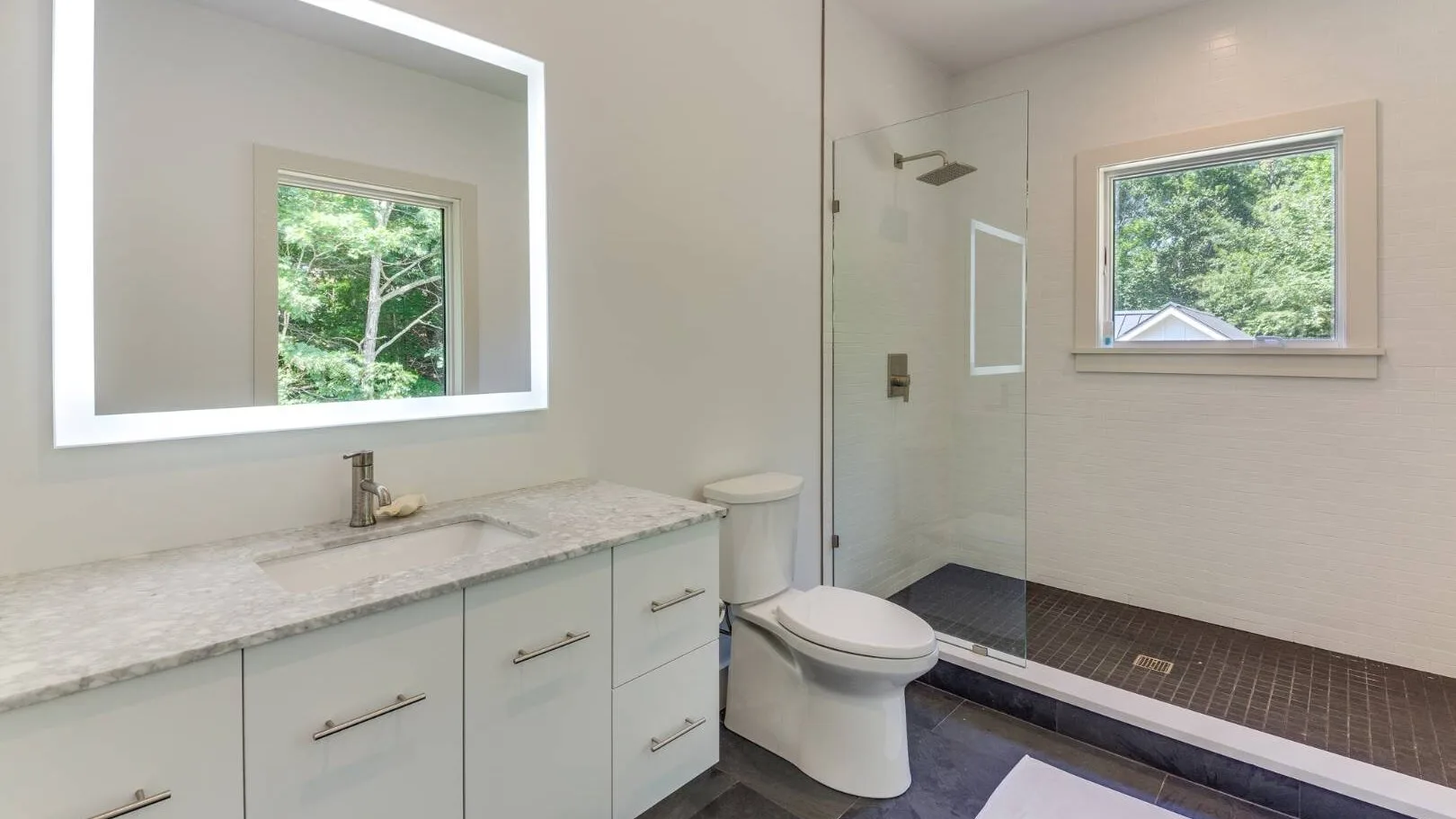 Un baño con un mueble largo, inodoro y ducha de vidrio.