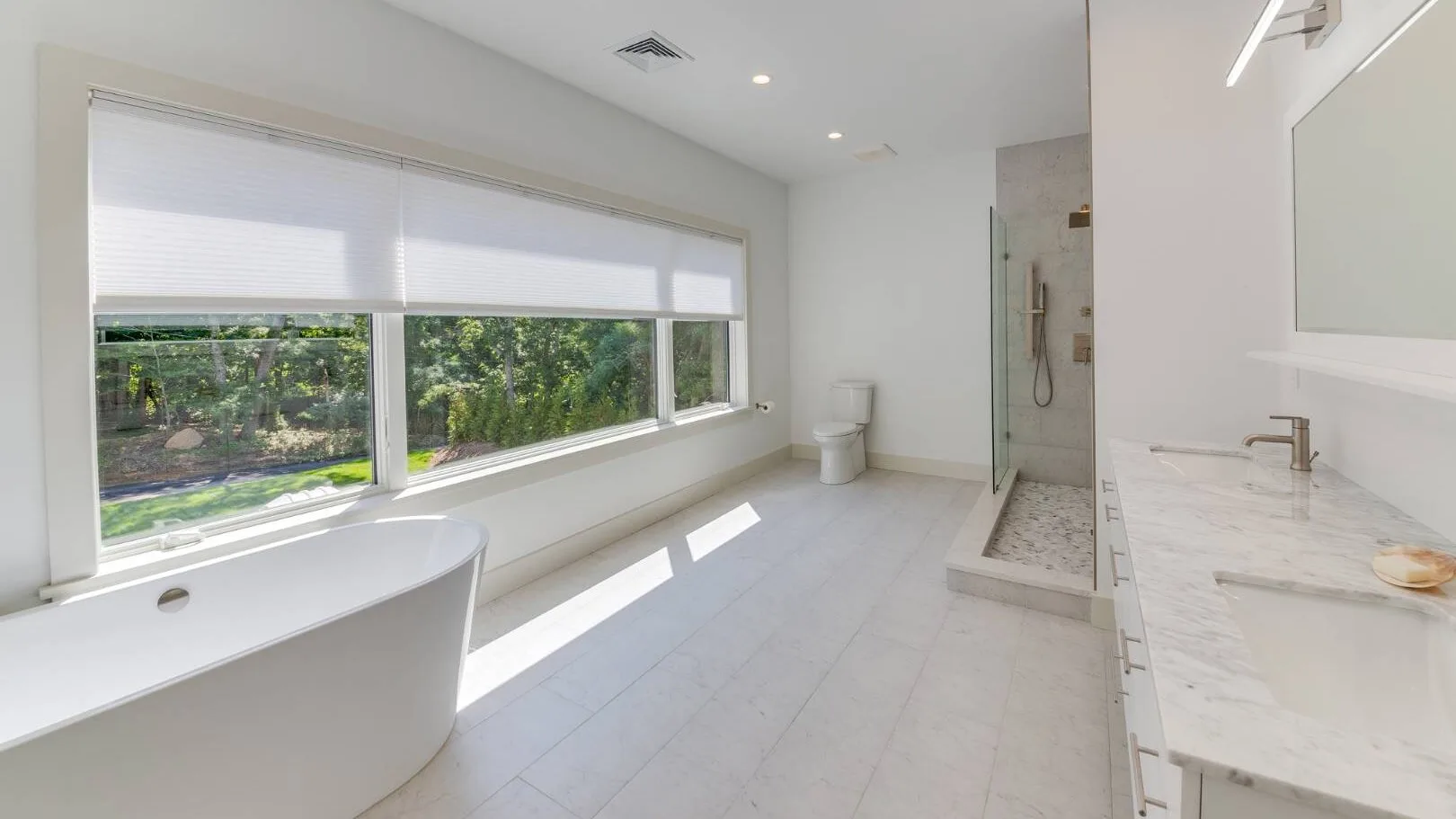 Un baño luminoso con bañera, ducha a ras de suelo y ventanas alargadas.