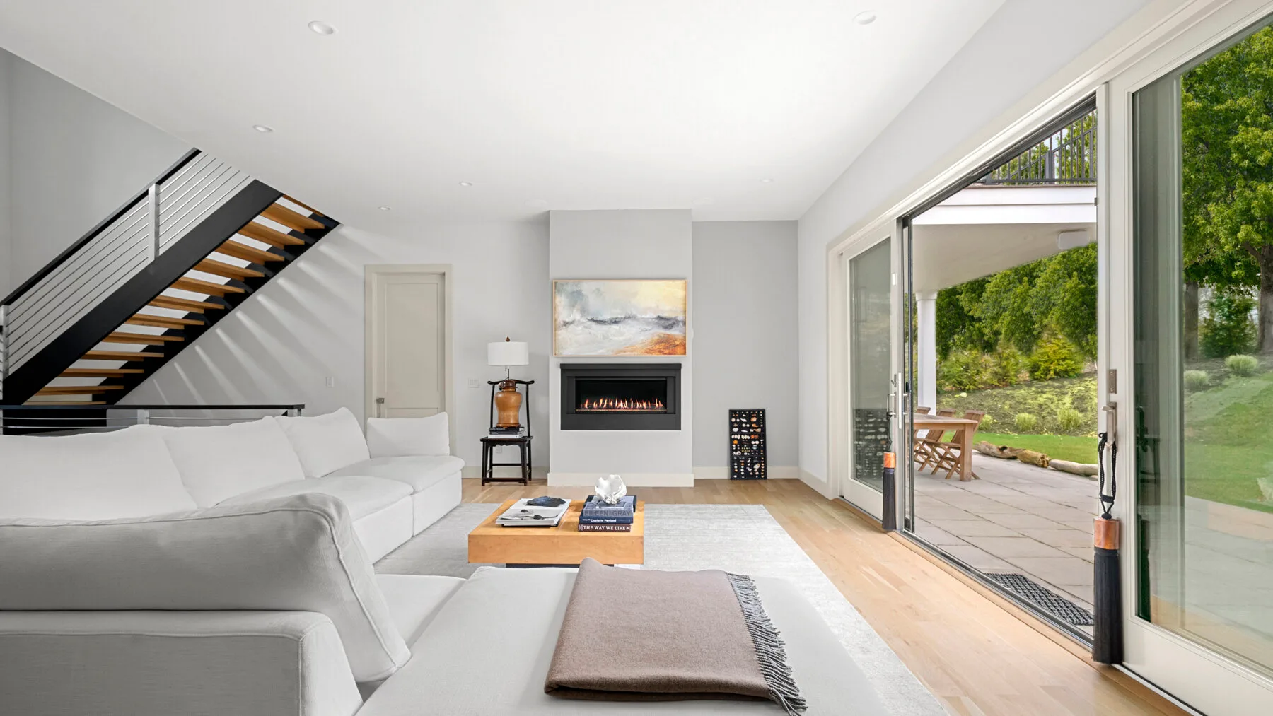 Una sala luminosa con asientos blancos, una chimenea y grandes ventanales hacia un patio.