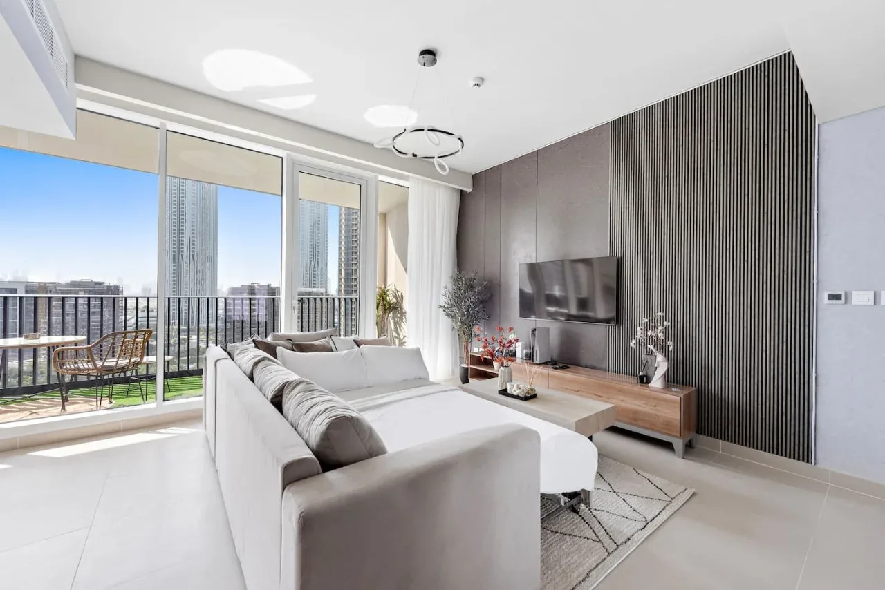 Una sala luminosa con asientos frente a un televisor y ventanas de piso a techo.