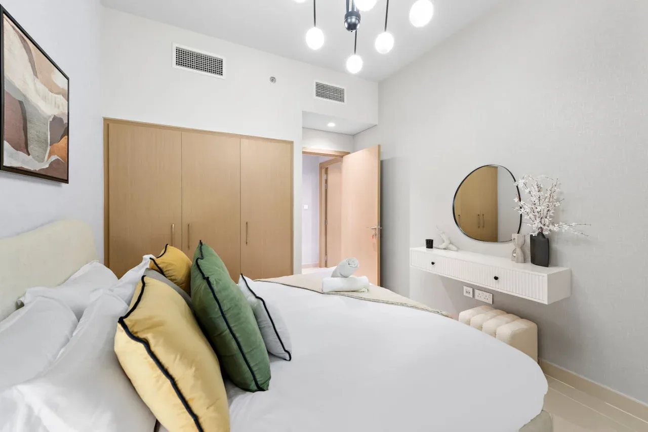 Un dormitorio luminoso con una cama, almohadas de colores y un tocador flotante.