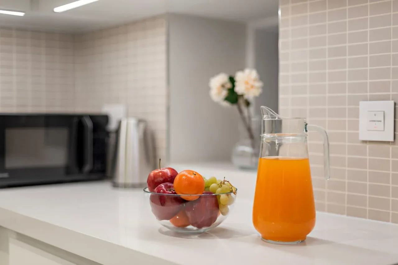 Una encimera de cocina muestra una jarra de jugo de naranja y un frutero.