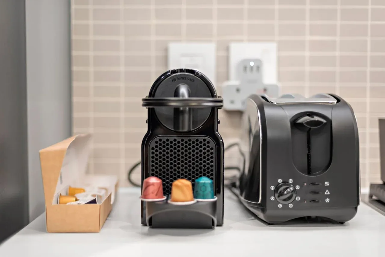 Una encimera de cocina muestra una cafetera de cápsulas junto a una tostadora.