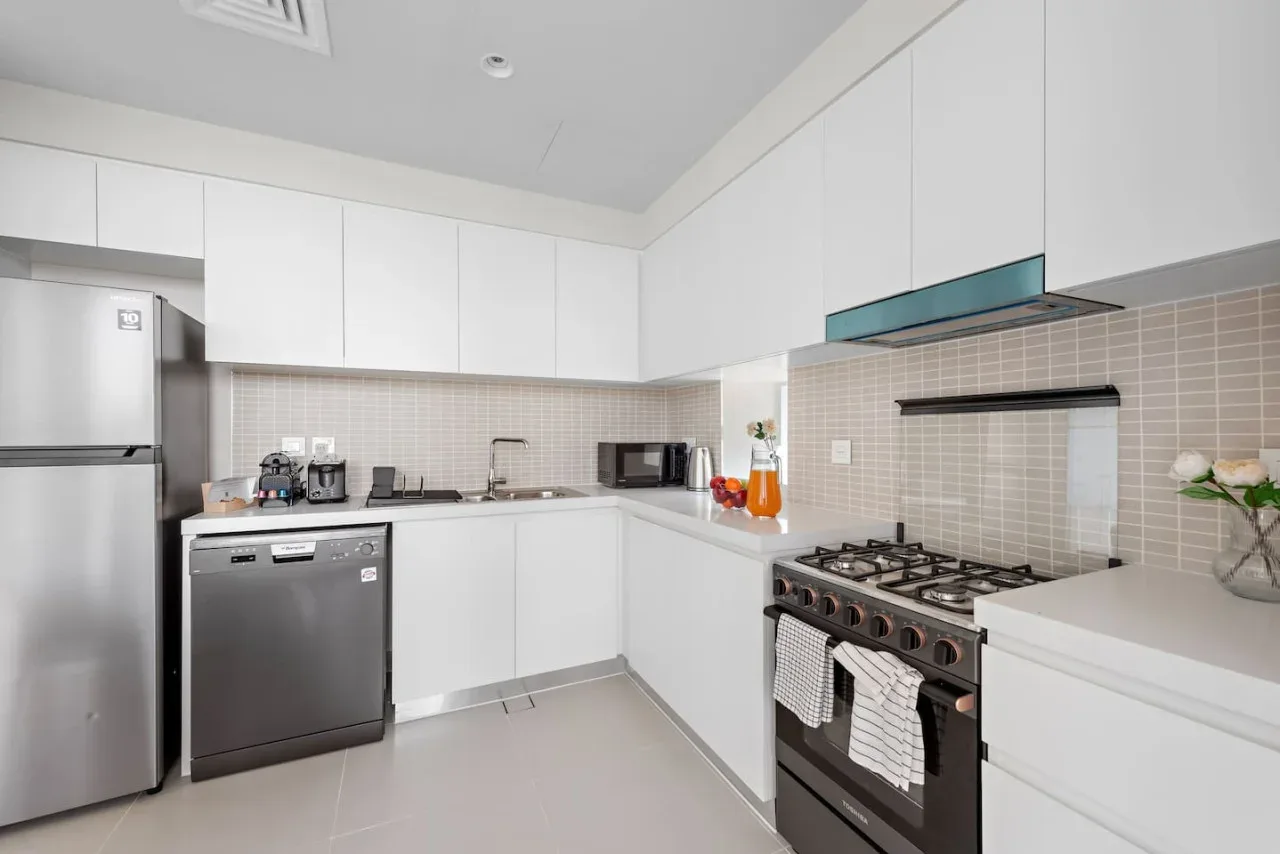 Una cocina moderna con gabinetes blancos, electrodomésticos de acero inoxidable y una estufa de gas.