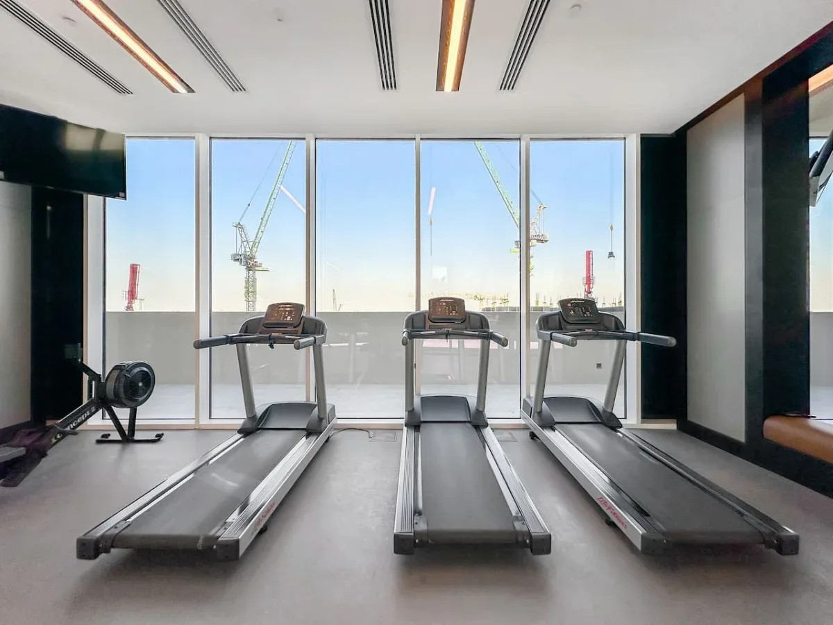 Un gimnasio con cintas de correr frente a grandes ventanales.