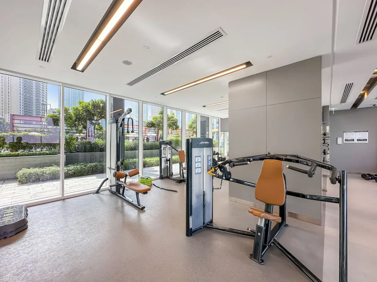Un gimnasio luminoso con máquinas de ejercicio junto a grandes ventanales.