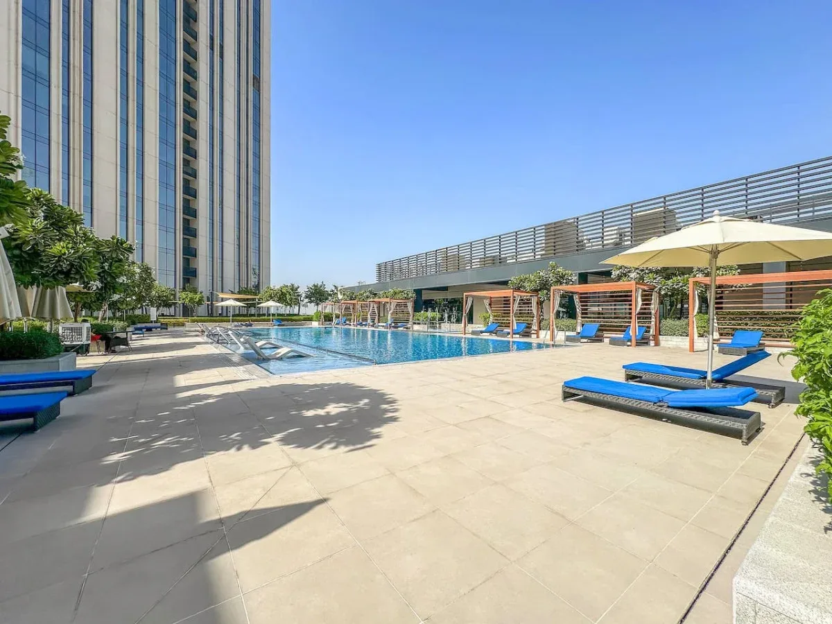 Una piscina al aire libre con tumbonas azules en una terraza soleada.