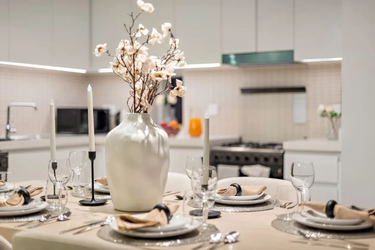 Una mesa puesta con platos y flores está en una cocina luminosa.