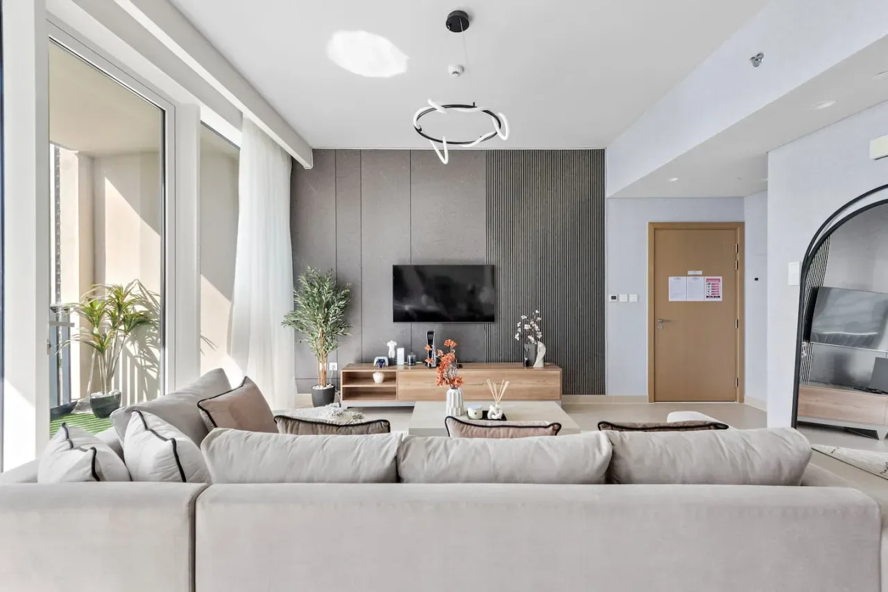 Una sala luminosa con asientos frente a un televisor en la pared y grandes ventanas.