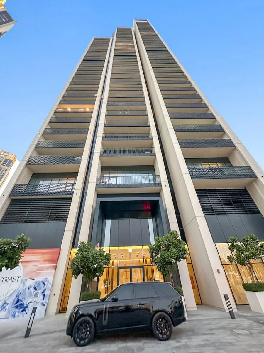 Un edificio moderno y alto se eleva sobre una entrada a nivel de calle y un automóvil estacionado.